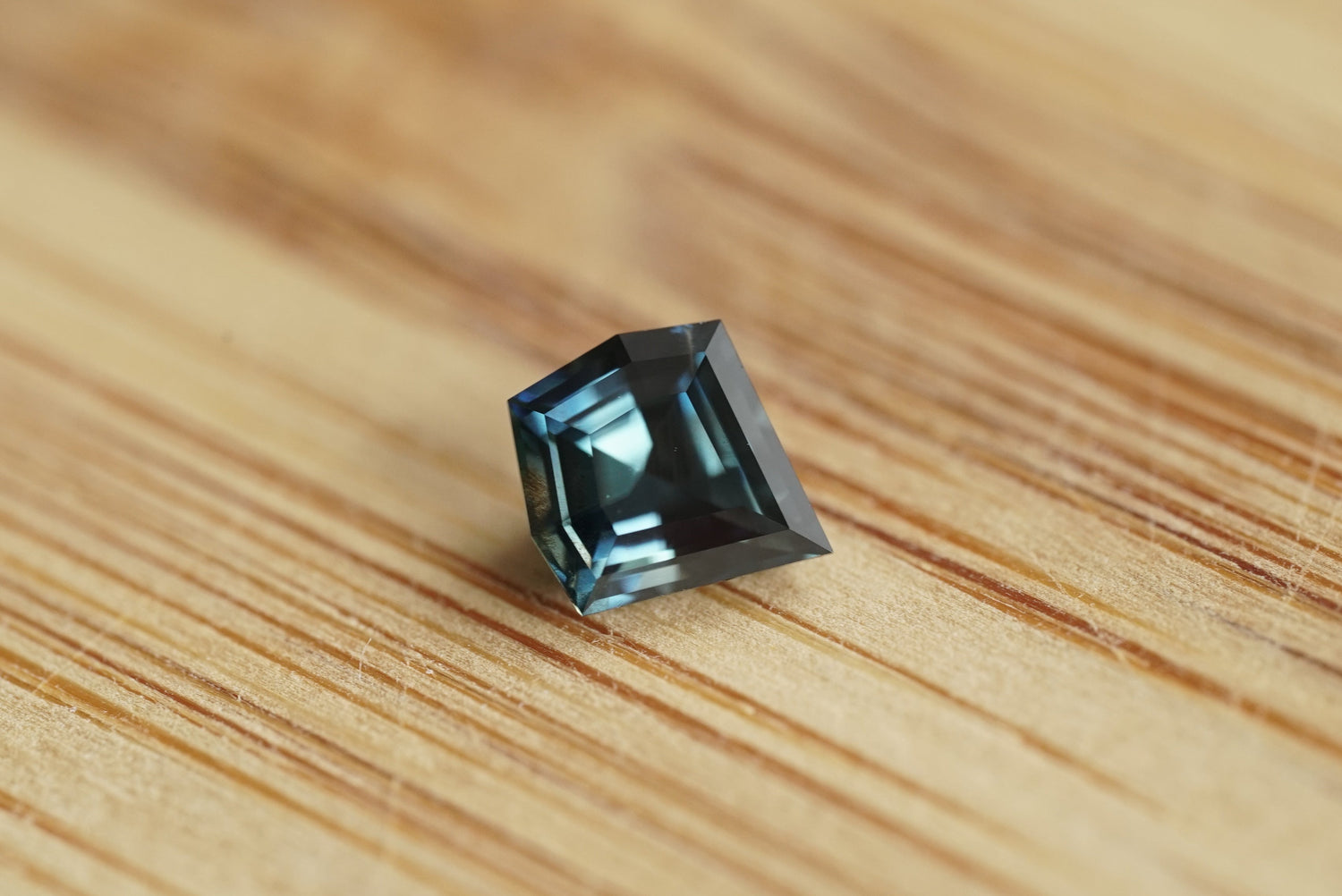 Faceted teal sapphire gemstone on a wooden surface