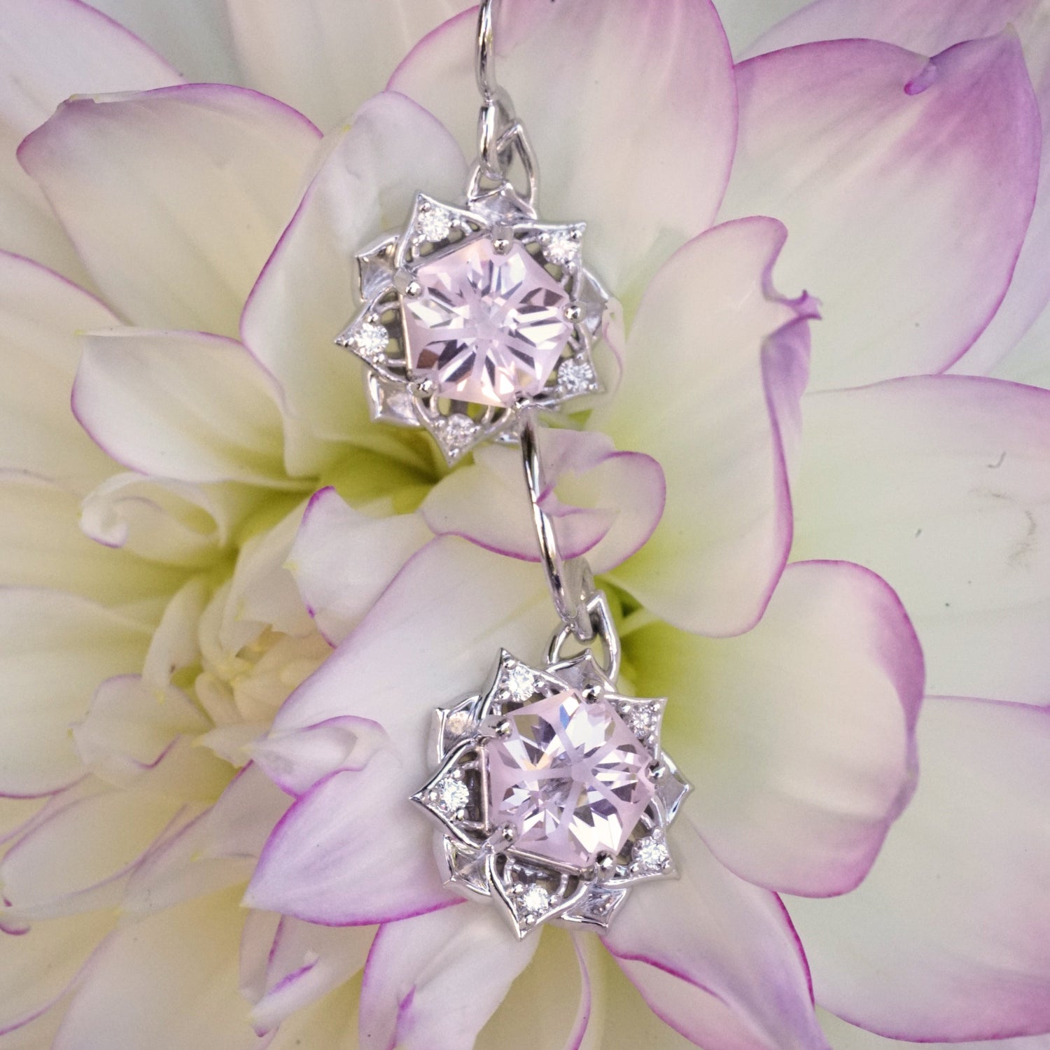 a pair of white gold earrings with a synthetic yag center stone and diamond accents rests on a pink and yellow flower