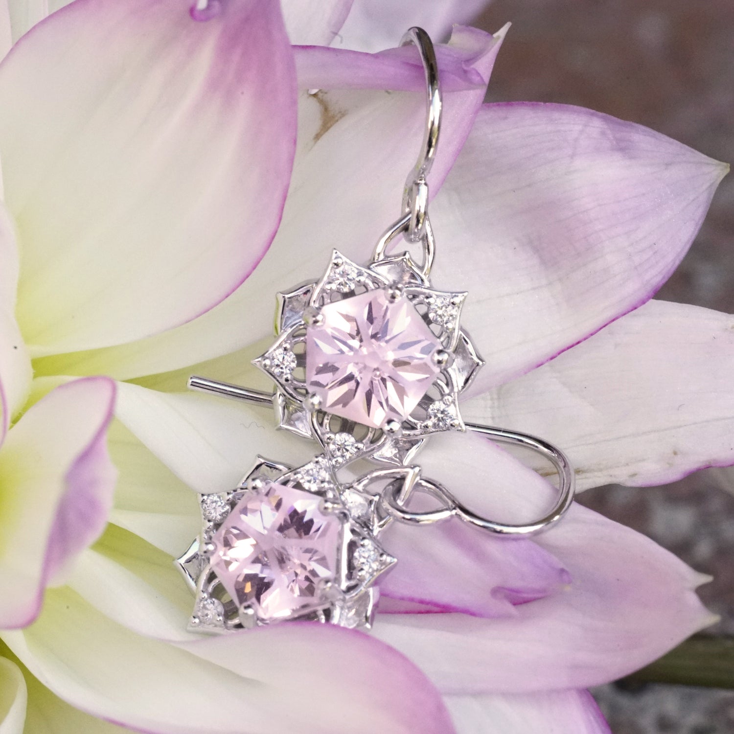 a pair of white gold earrings with a synthetic yag center stone and diamond accents rests on a pink and yellow flower
