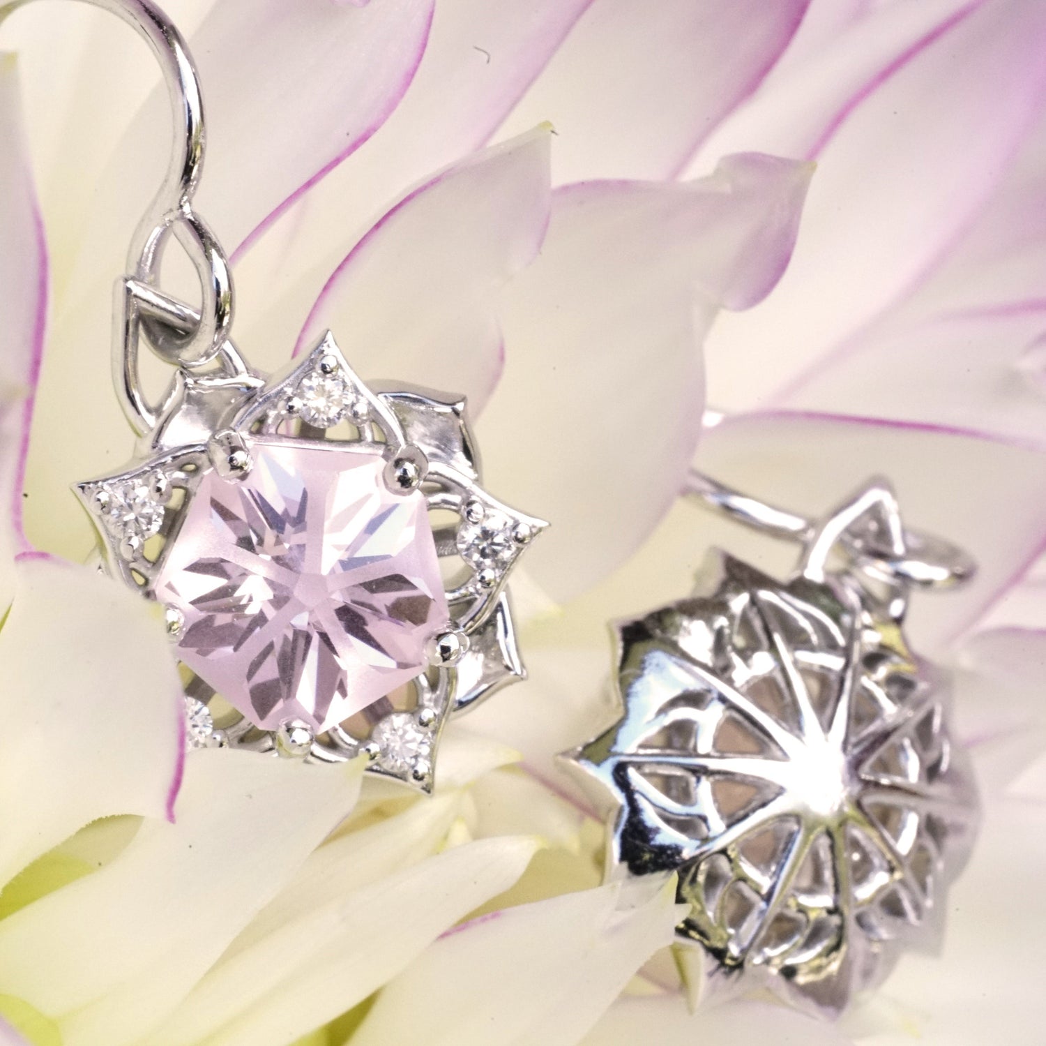 a pair of white gold earrings with a synthetic yag center stone and diamond accents rests on a pink and yellow flower
