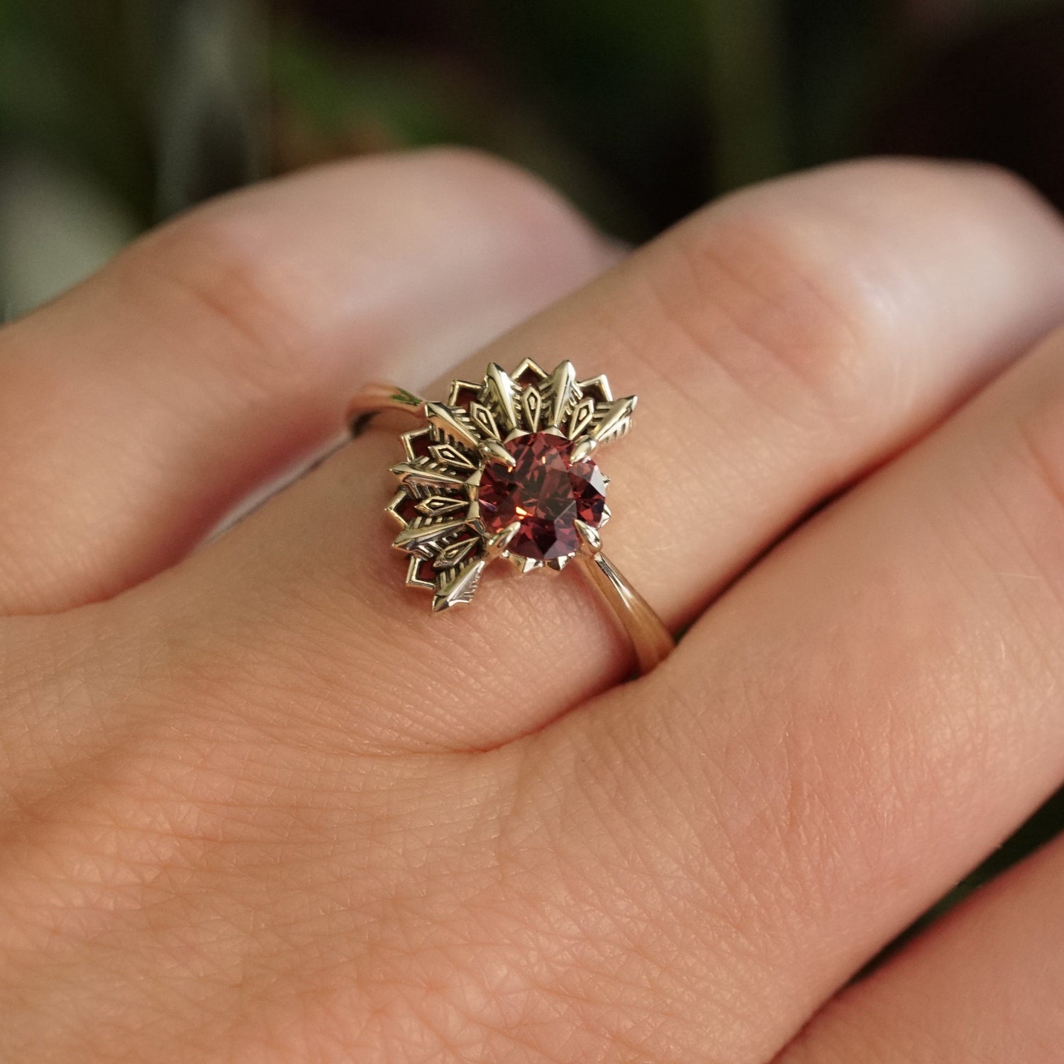 Gold deco ring with a Lindi Garnet on a person's finger against a blurred background