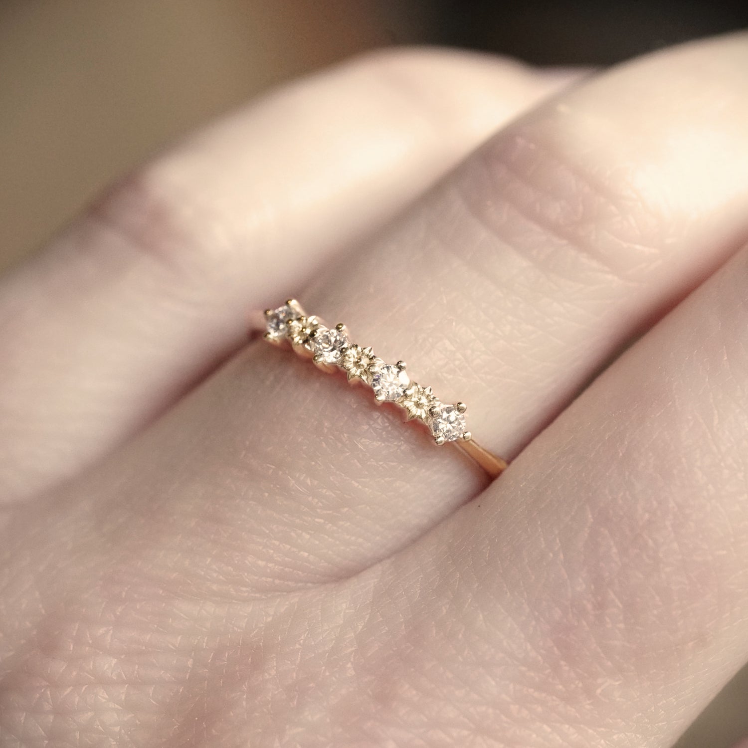 Yellow gold ring with small diamonds on a finger against a blurred background