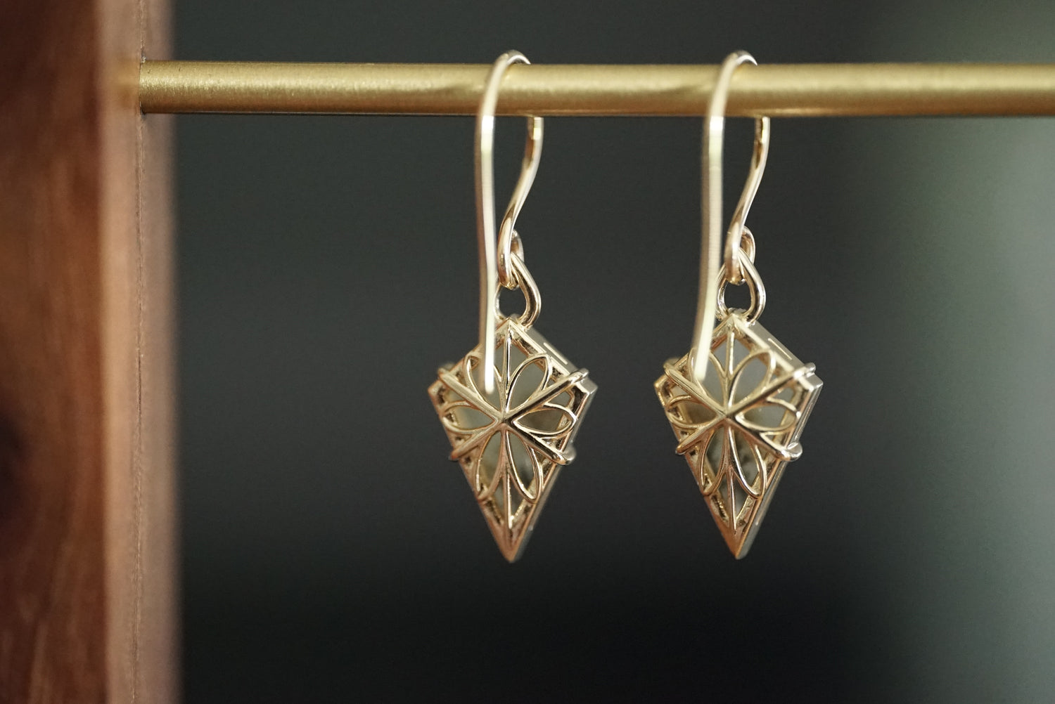 Gold diamond-shaped earrings on a dark background