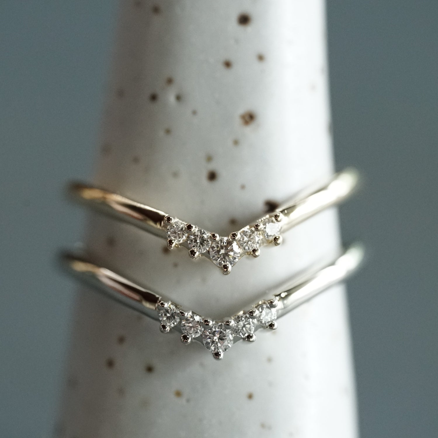 A white gold and diamond V shaped shadow style wedding band and a yellow gold and diamond V shaped shadow style wedding band on a white ceramic display