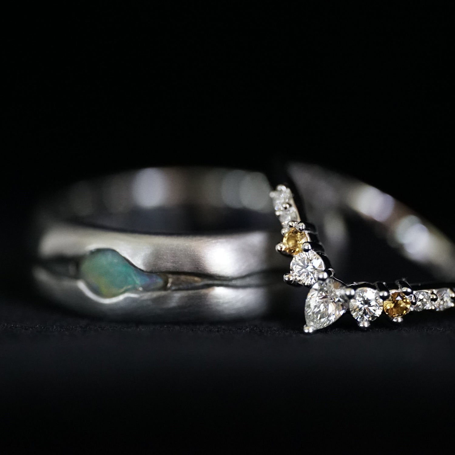 a custom wedding set in white gold featuring an opal the gents band and diamonds a citrine in the ladies band on a black background