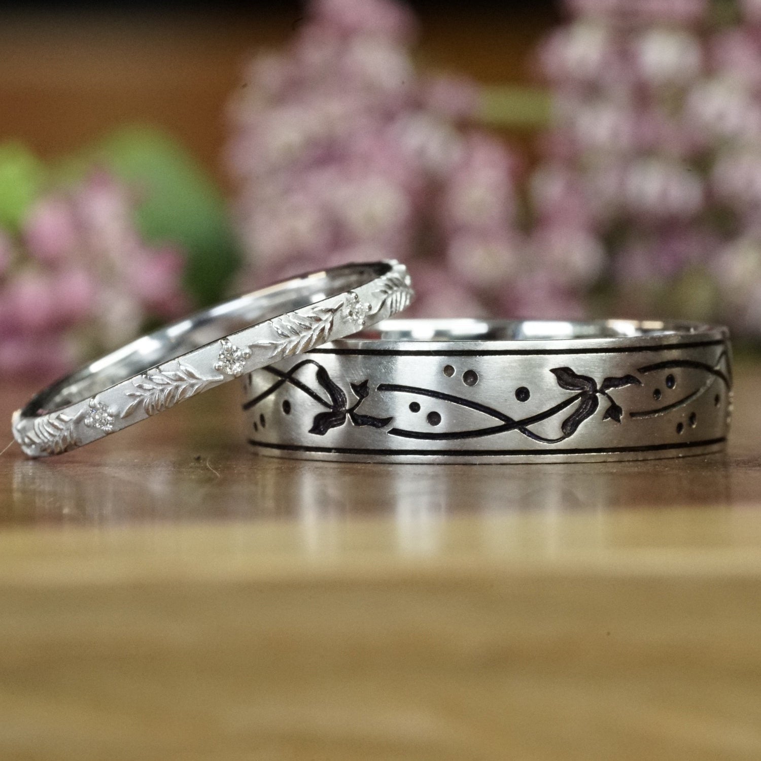 a custom white gold and diamond wedding set on a wooden display in front of pink flowers