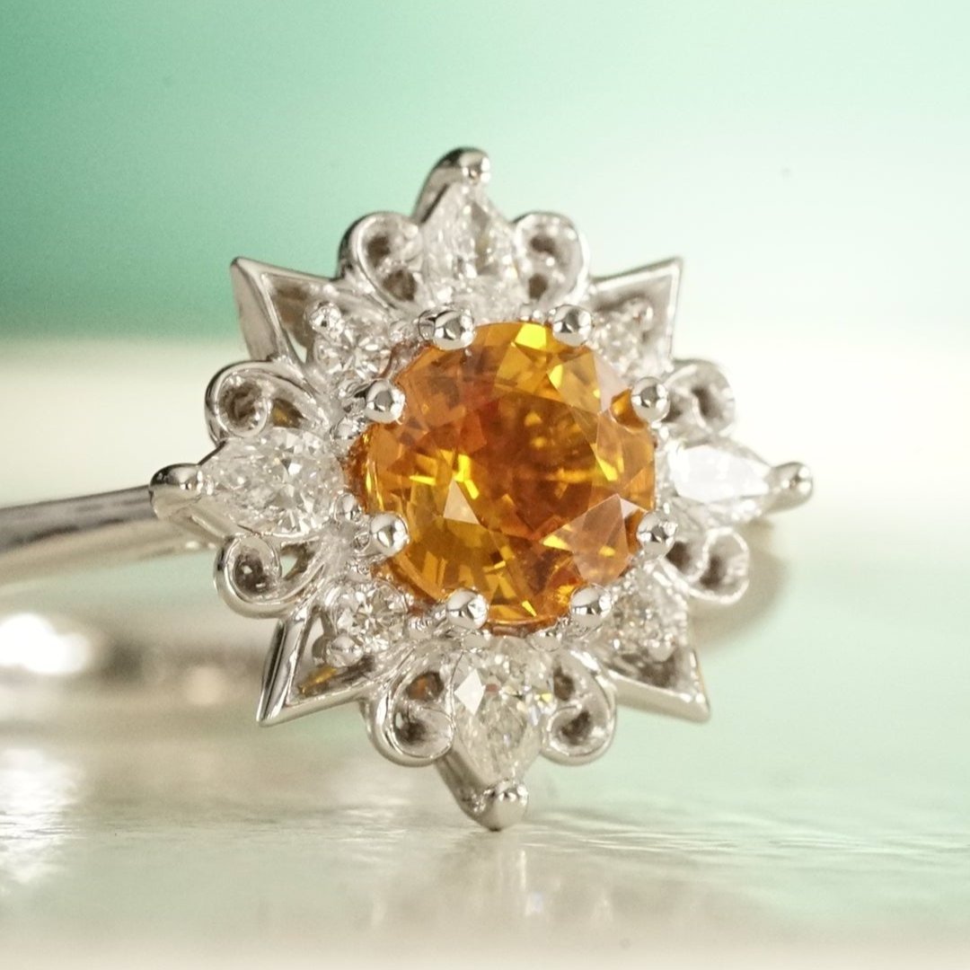 a white gold diamond and vibrant orange sapphire engagement ring shown on a glossy white background