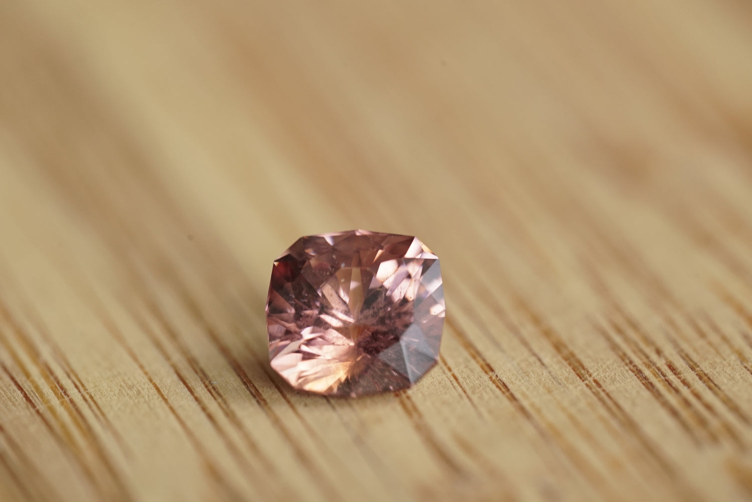 Faceted pink zircon gemstone on a wooden surface