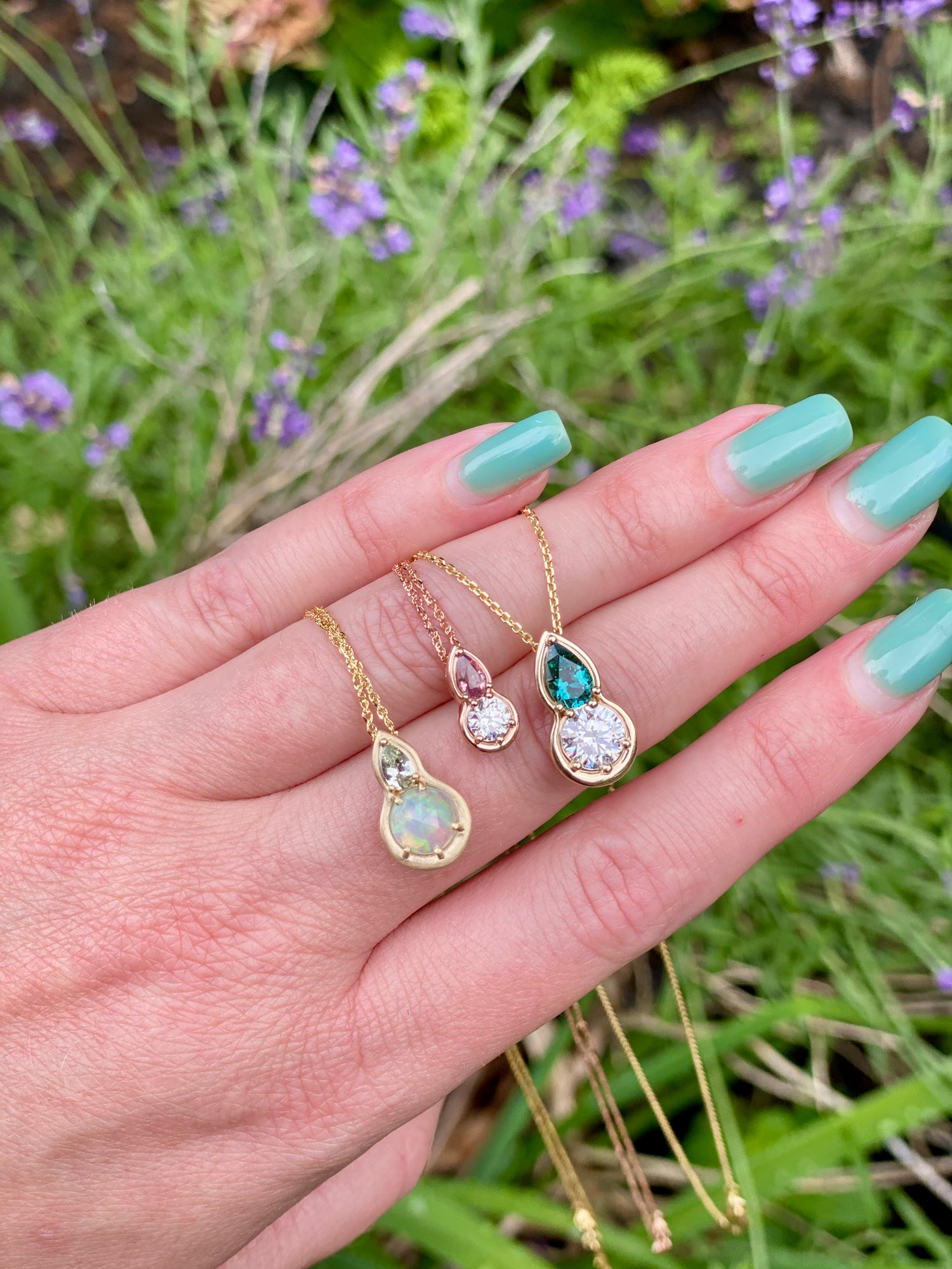 Hand holding three gold necklaces with gemstones against a natural background