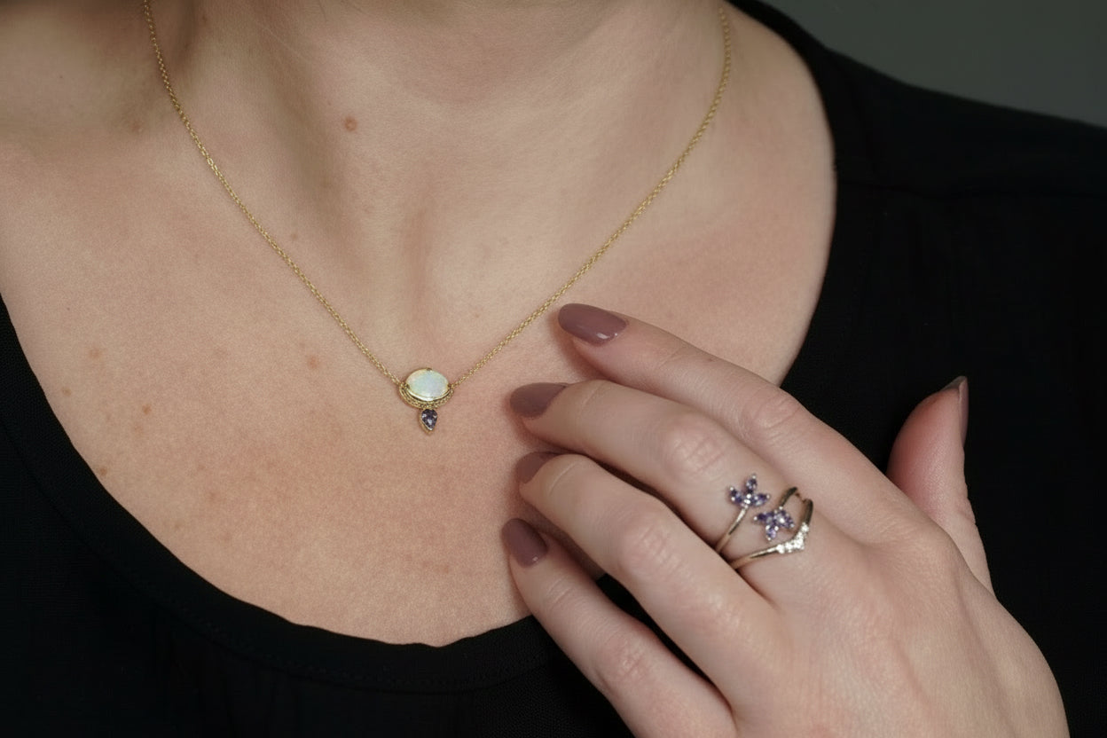 Necklace with a pendant and a ring with a floral design on a person's hand.