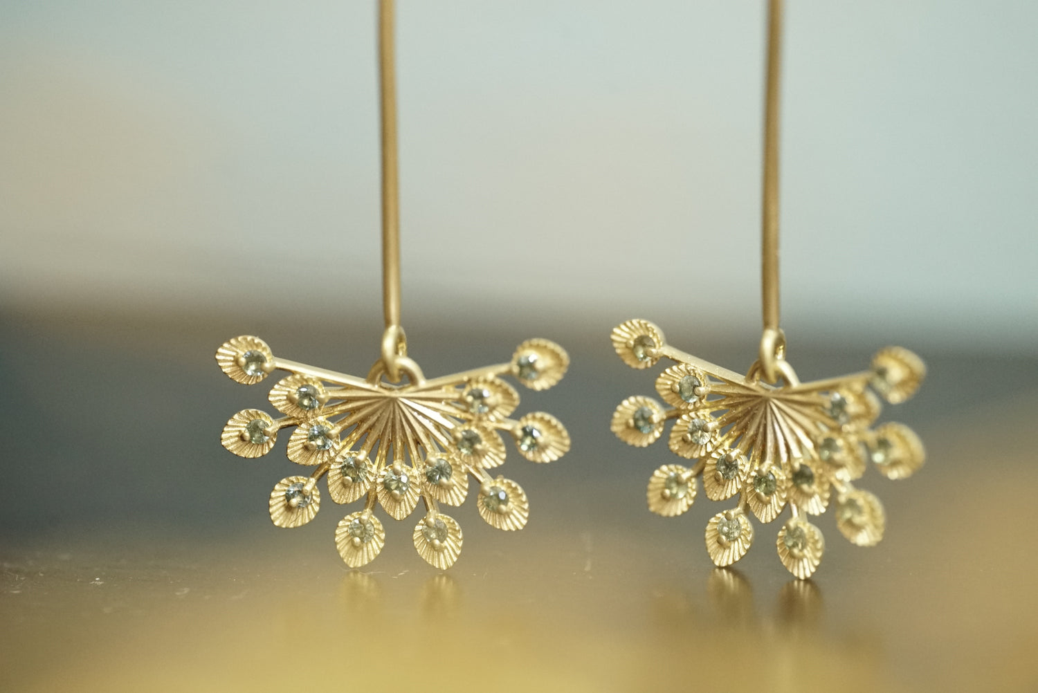 a pair of 14k yellow gold and teal sapphire drop earrings on a glossy blue and yellow background