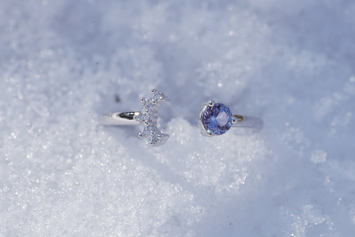 A white gold, sapphire, and diamond ring rests lightly in the snow