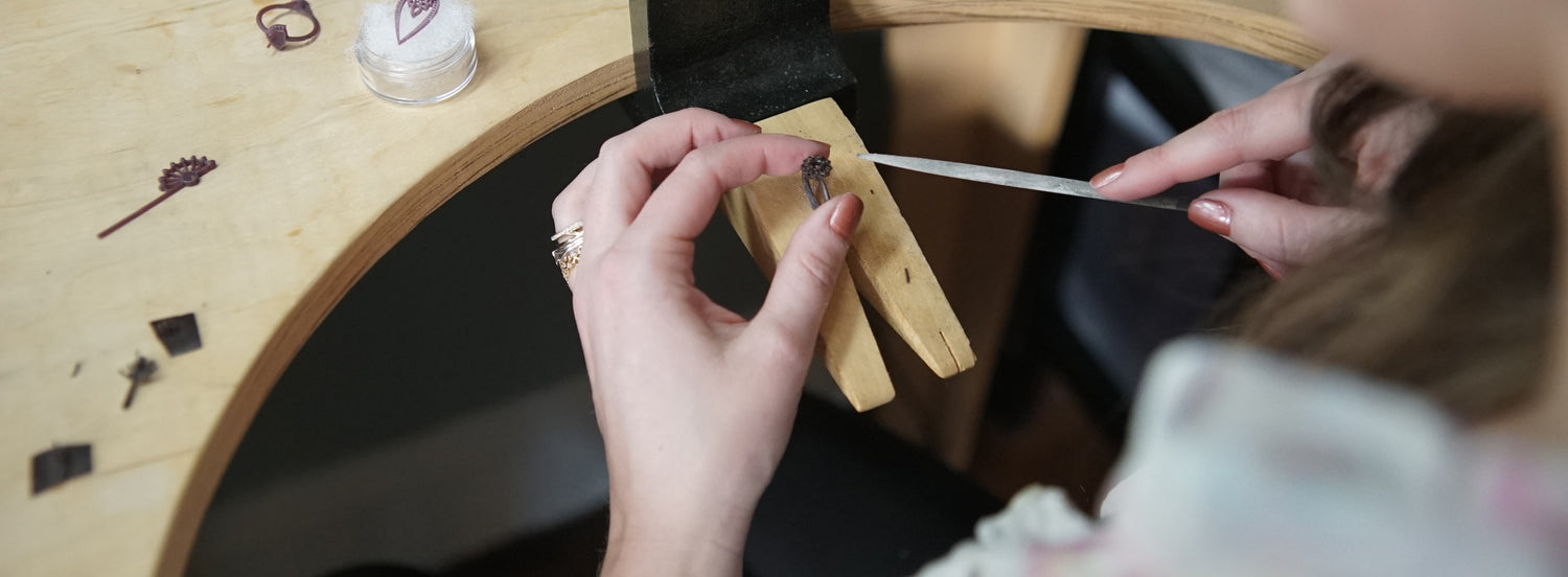 A light skinned brunette files 3d printed wax models on a wooden bench