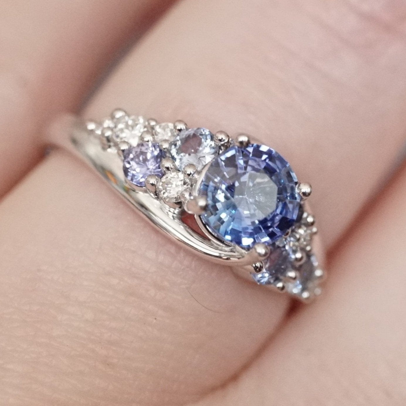 a white gold engagement ring with a gorgeous blue sapphire center stone and blue sapphire and diamond accents shown on a light skinned left hand