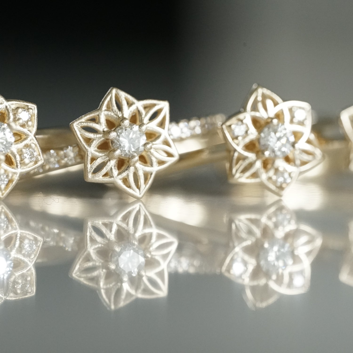 a macro photo of daffodil inspired yellow gold and diamond rings on a reflective background