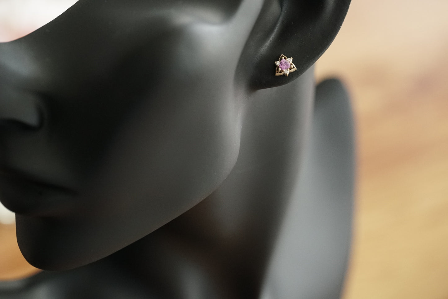 a pair of yellow gold triangular shaped studs featuring a pink sapphire trillion center stone and 3 round diamond accents shown on a manikin for scale