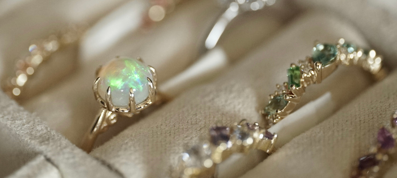 multiple rings are shown in a jewelry box with the main focus on a yellow gold and opal ring