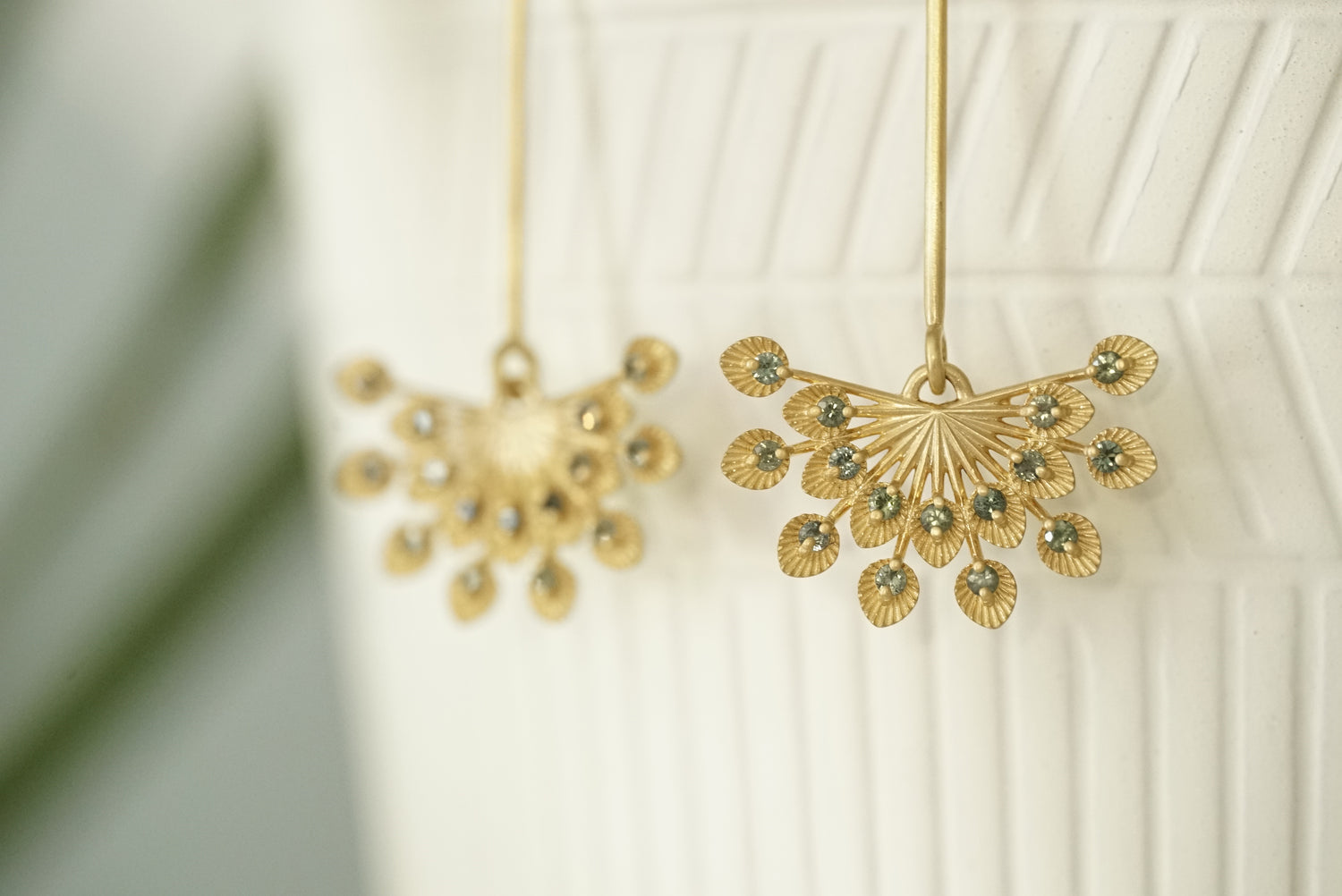 a pair of 14k yellow gold and teal sapphire drop earrings in front of a matte white ceramic display