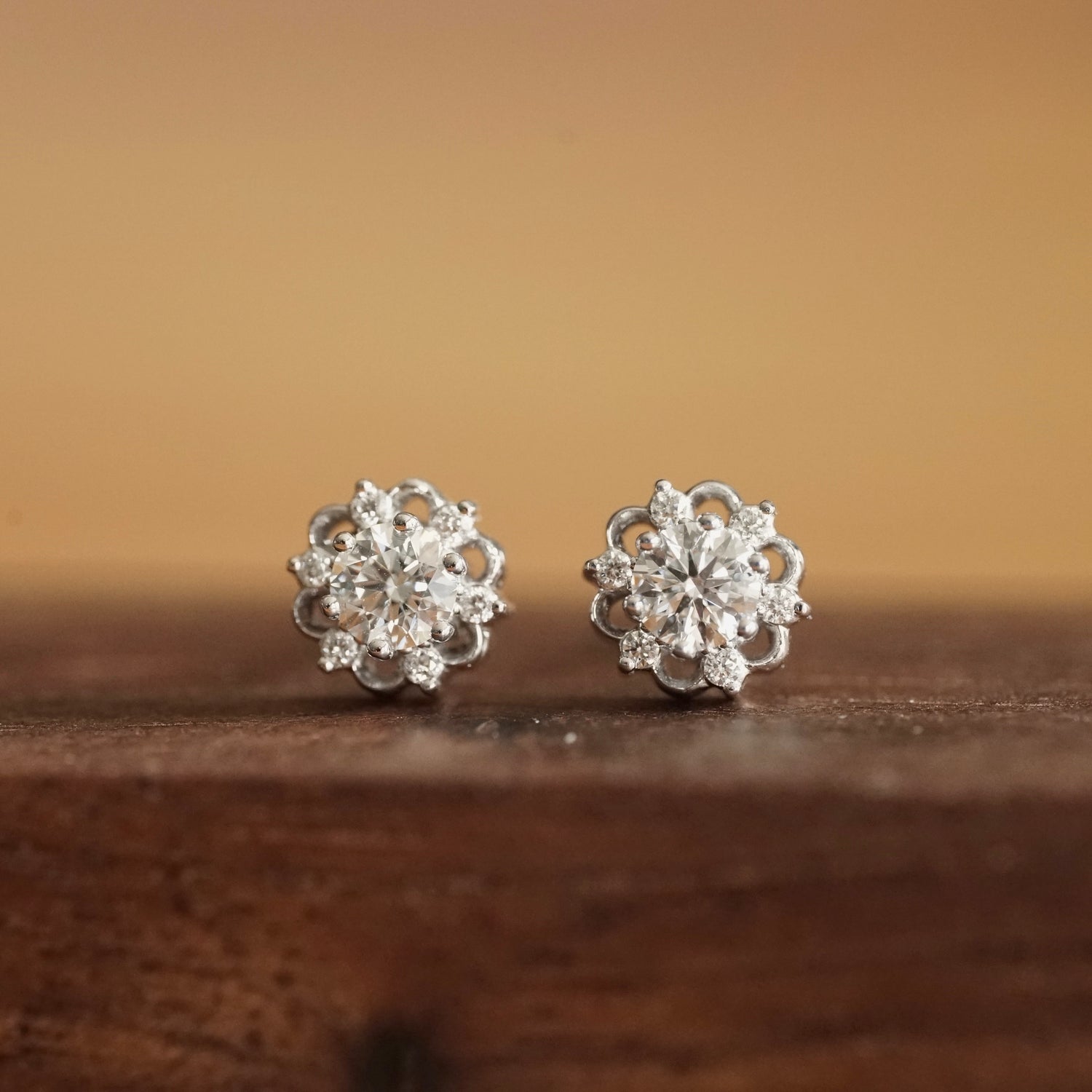 a pair of white gold stud earrings with a lab ground diamond center stone and 6 natural diamond accents rests on a wood base