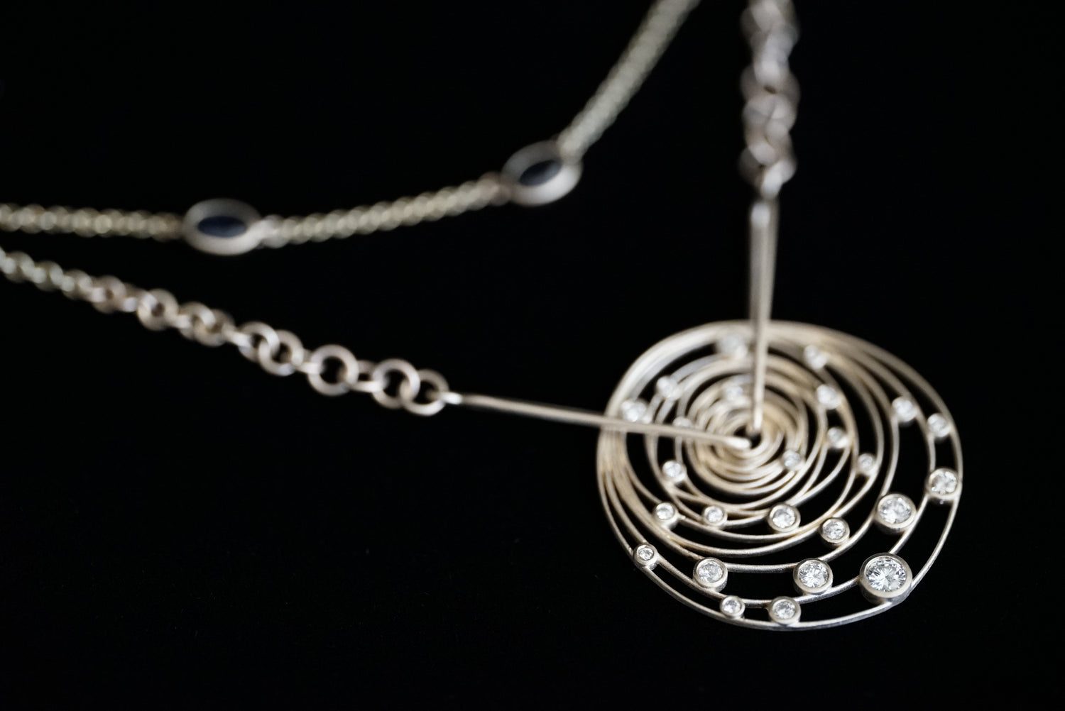 A gold necklace with a spiral pendant on a black background