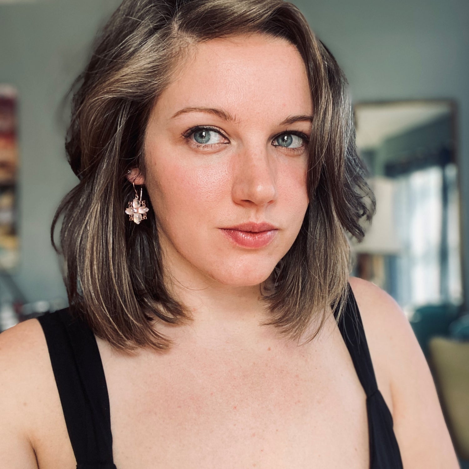 A light-skinned brunette with blue eyes wearing 14K Rose Gold, purple sapphire, and rainbow moonstone drop earrings in a blue room