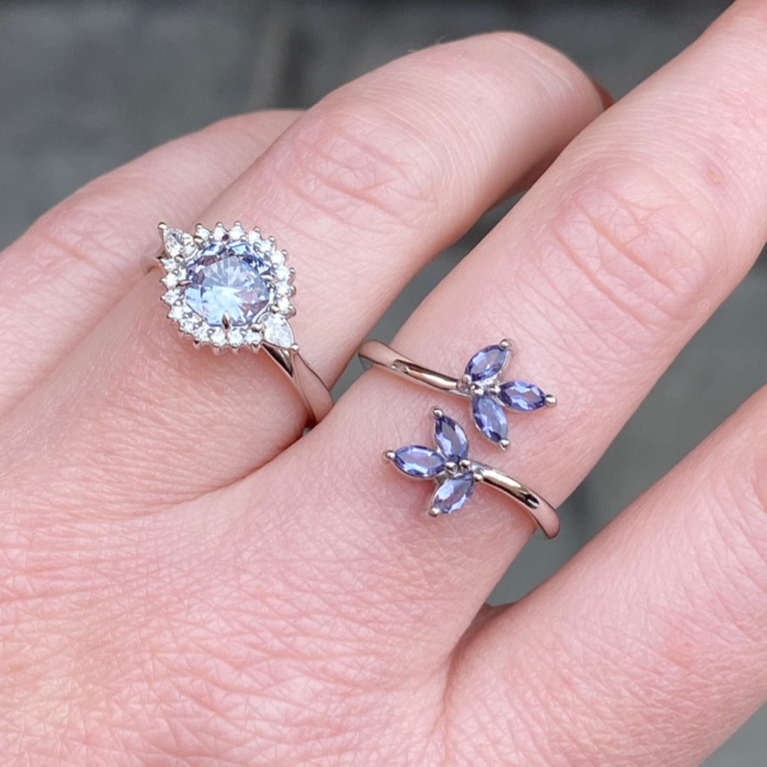 A white gold and purple polite leaf inspired ring and a lavender spinel and diamond halo style ring on a light-skinned left hand