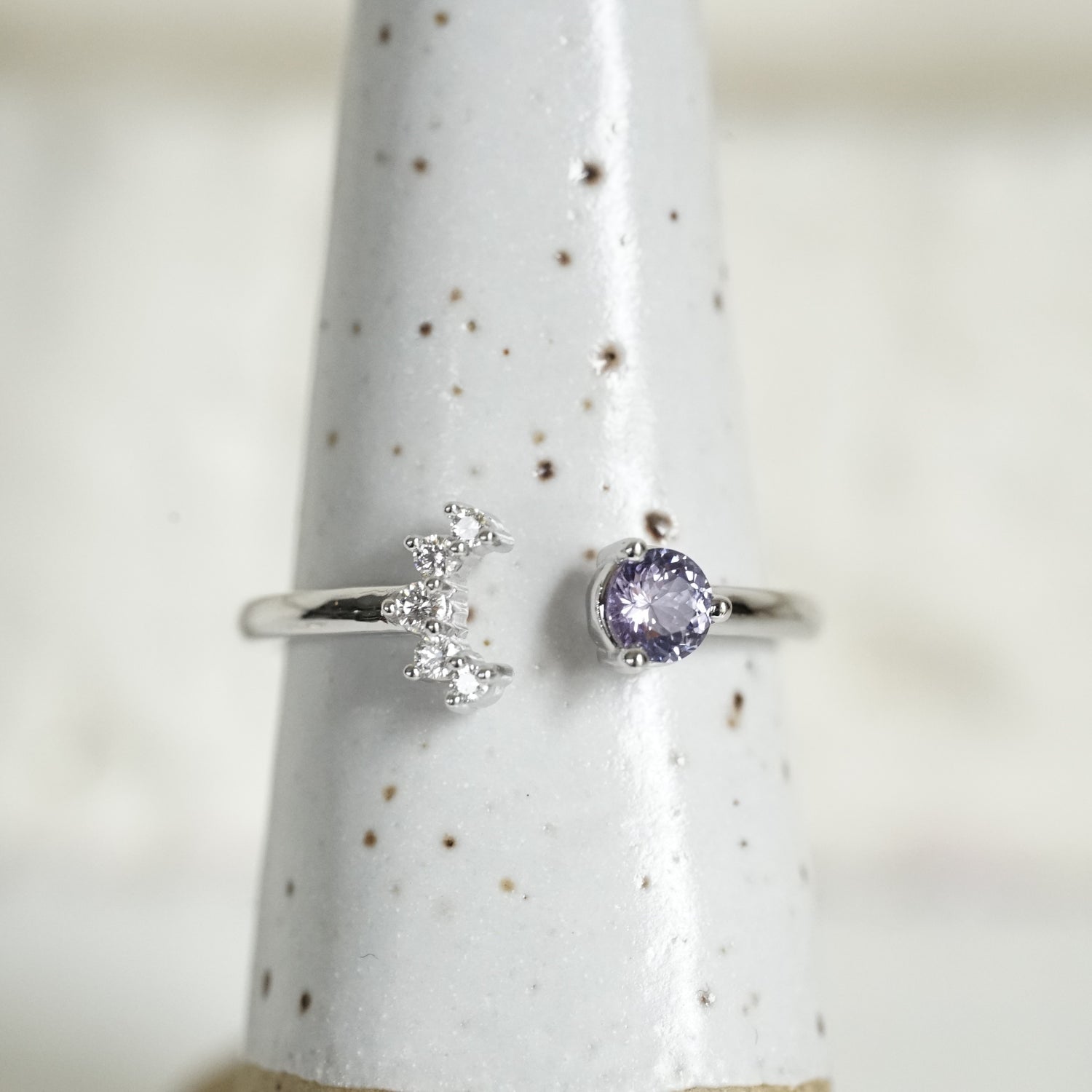 a white gold open style stacking ring with a light blue sapphire on the right and 5 diamonds on the left in a crescent shape on a white ceramic display