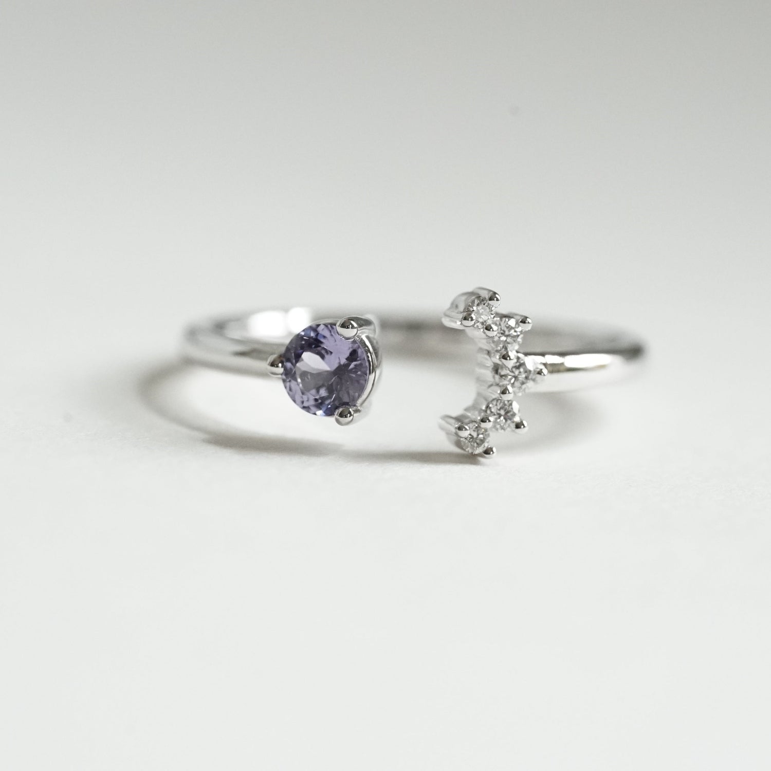 a white gold open style stacking ring with a light blue sapphire on the left and 5 diamonds on the right in a crescent shape on a white background
