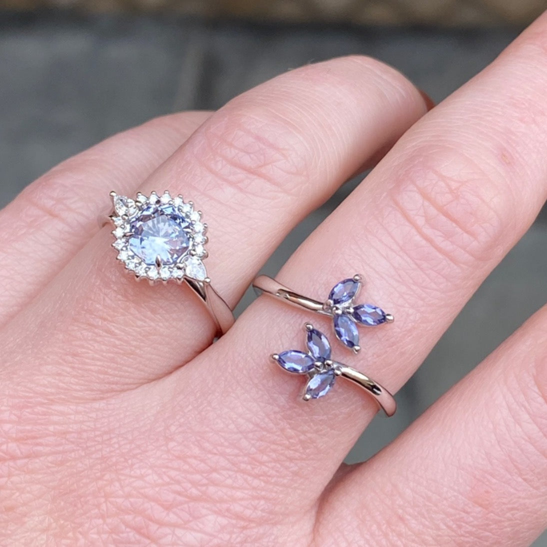A white gold and purple polite leaf inspired ring and a lavender spinel and diamond halo style ring on a light-skinned left hand