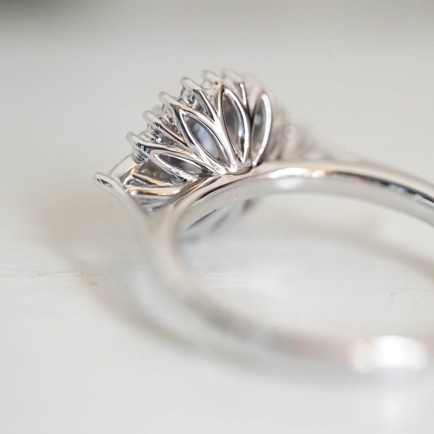 A macro photo of the floral inspired basket design on a custom white gold ring laying on a white background
