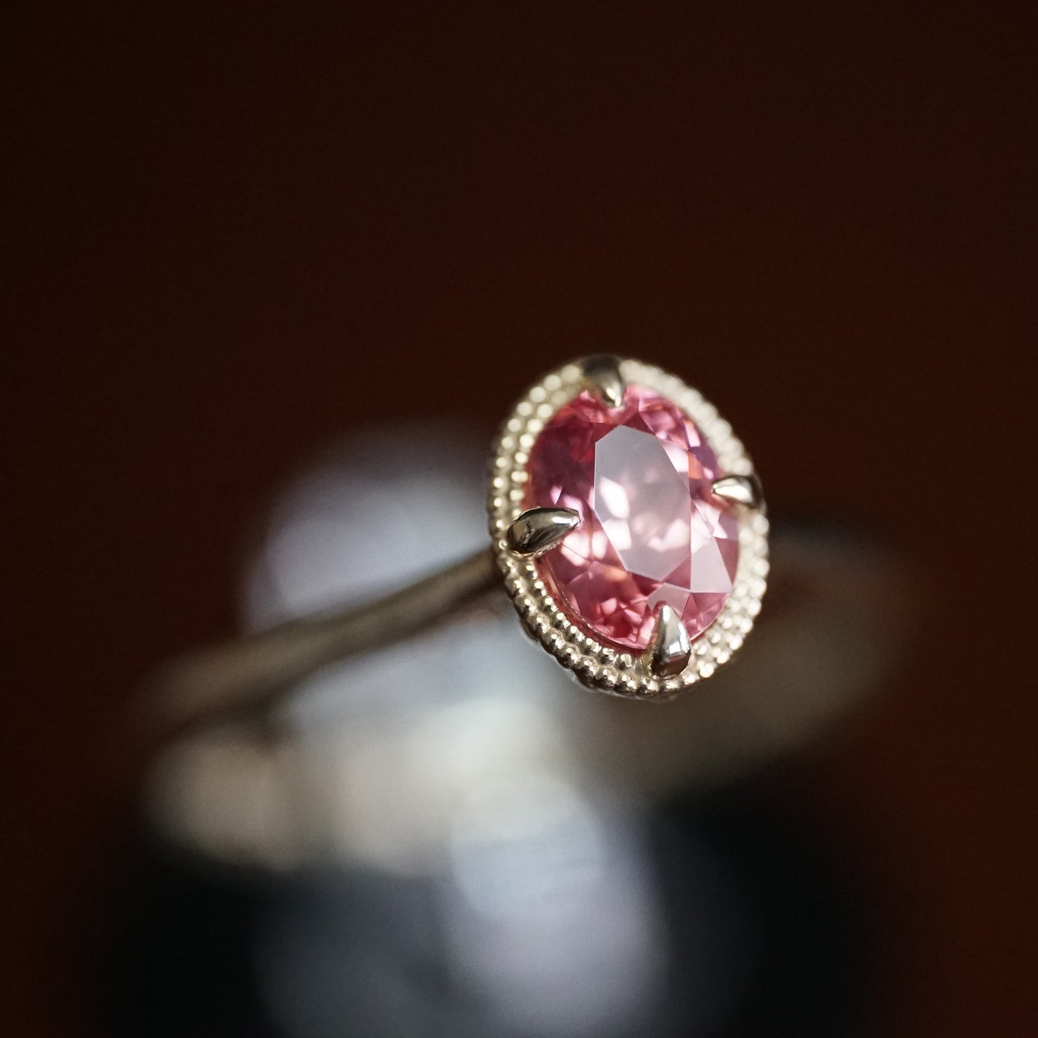 a macro photo of a vibrant pink spinel in a yellow gold ring setting with beaded halo design