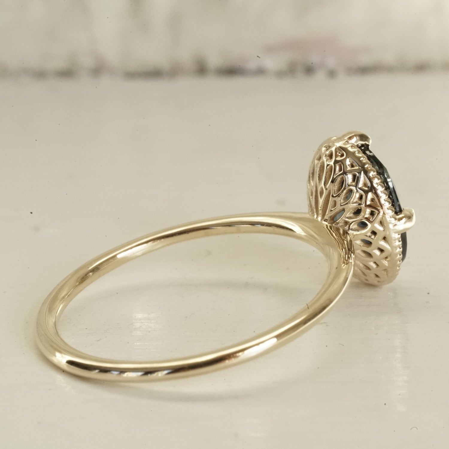 a yellow gold ring with an ornate open wirework basket on a glossy white background