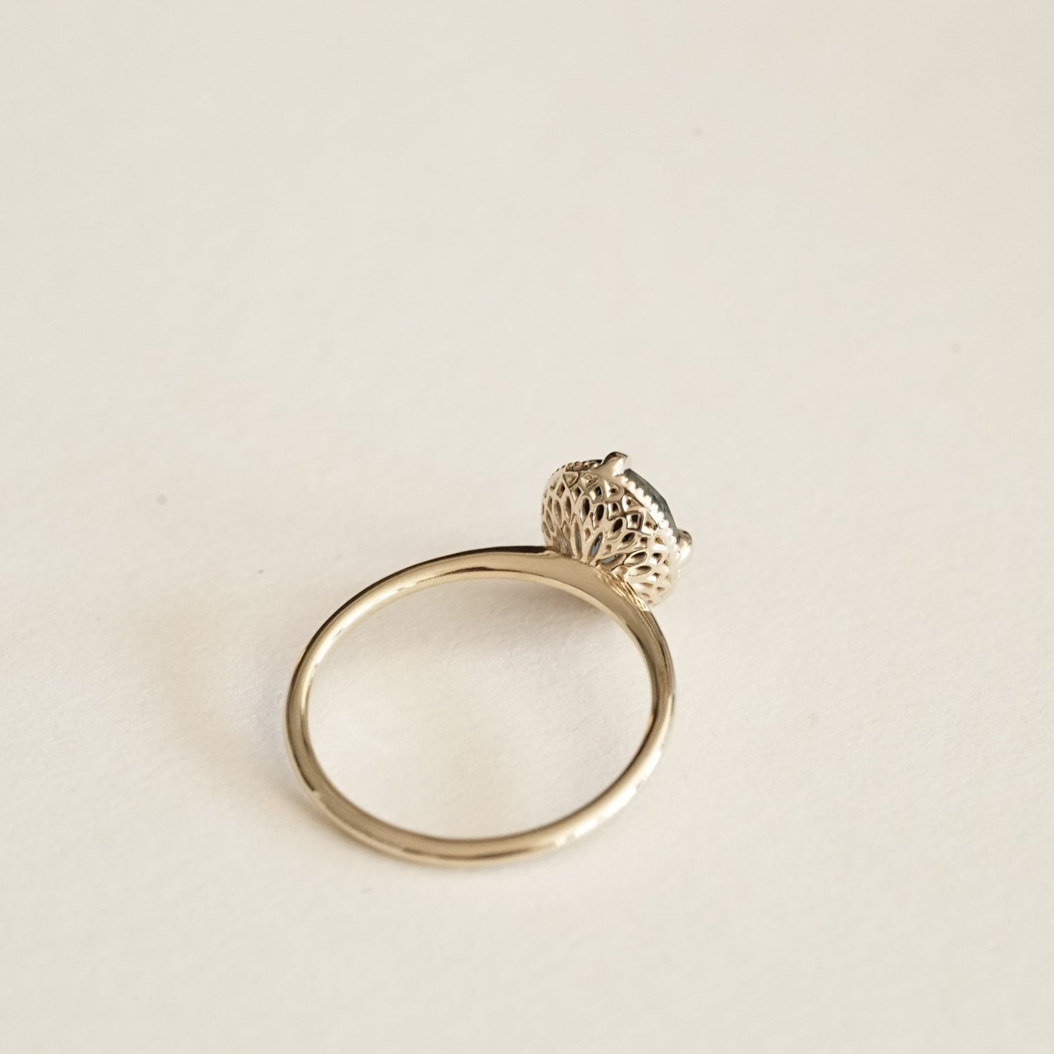 a yellow gold ring with an ornate open wirework basket on a matte white background