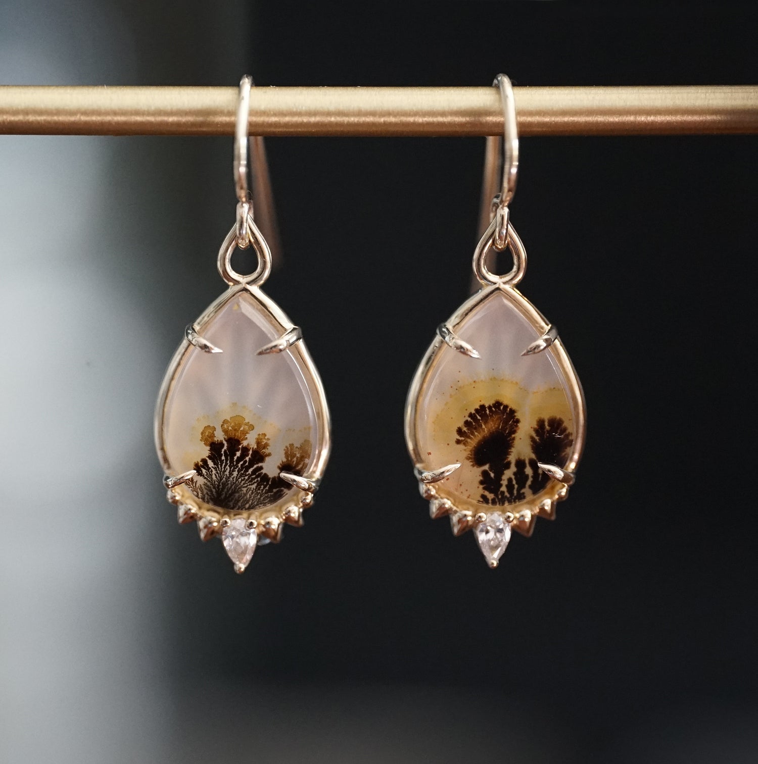 a pair of yellow gold drop earrings with dendritic agate center stones a single diamond accent at the base hang on a brass bar