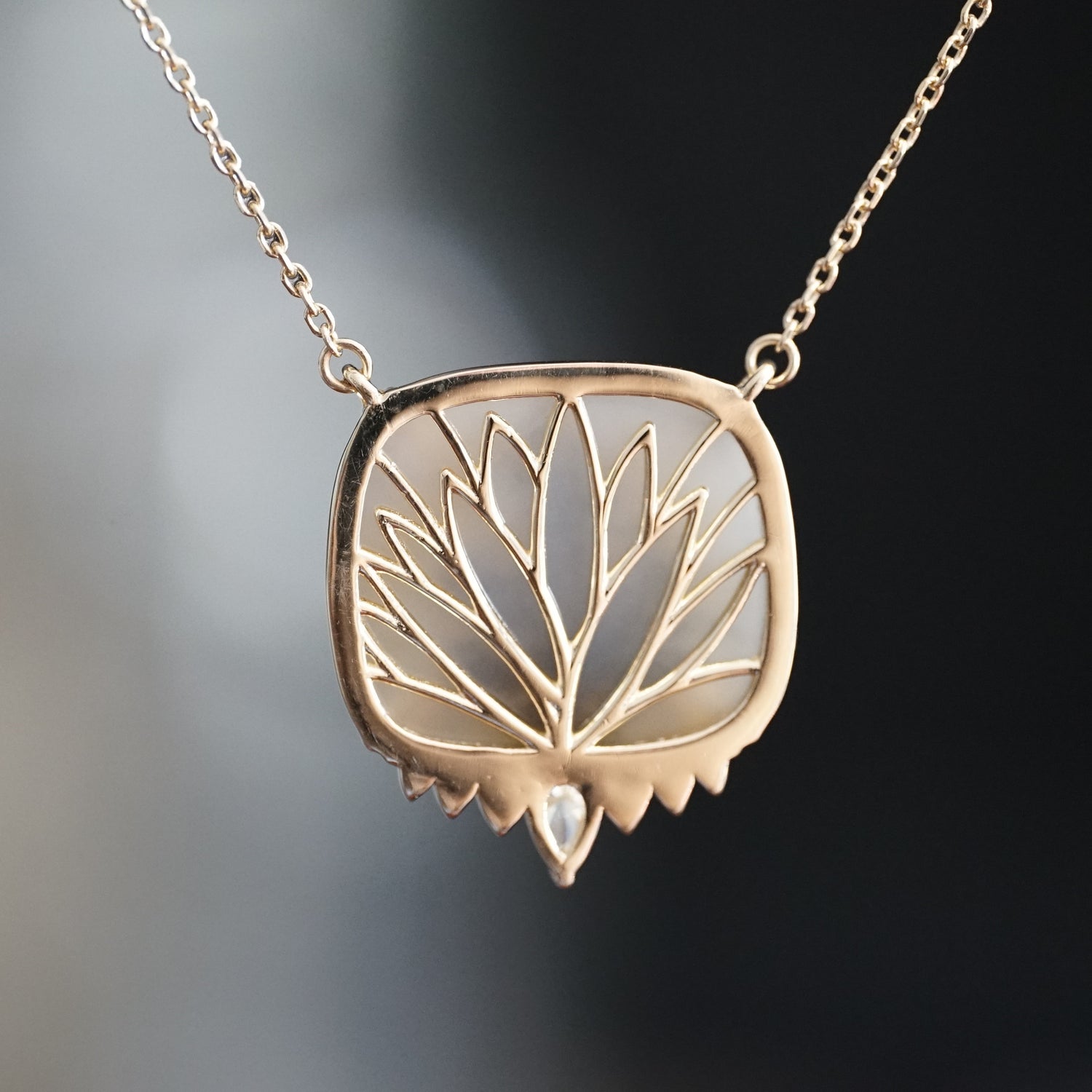 a yellow gold necklace with a dendritic agate in the center and single diamond accent at the base hangs on an open link chain and is rotated to show the leaf detailing on the back