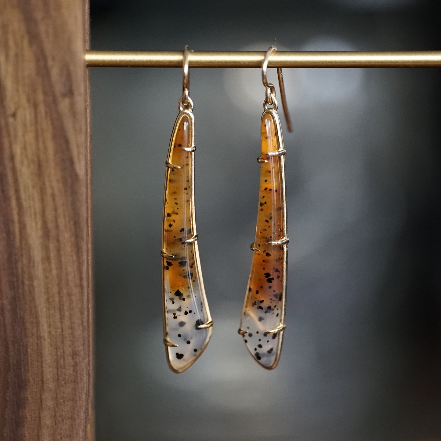 a pair of yellow gold earrings featuring elongated Montana agates which fade in color from yellow to clear and have natural black inclusions hanging on a brass bar