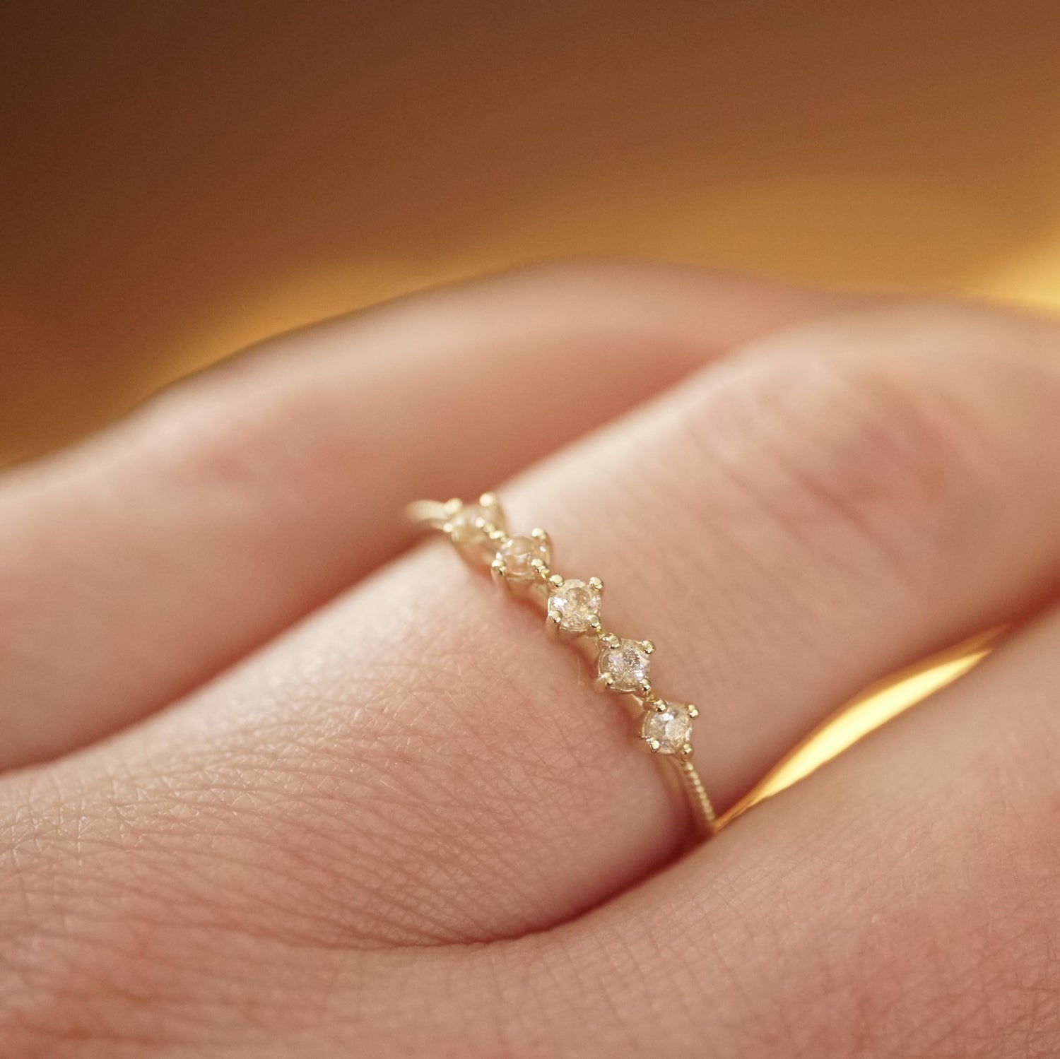 a yellow gold ring with 5 round light pink Oregon sunstones and migraine detail on the shank on a light skinned left hand