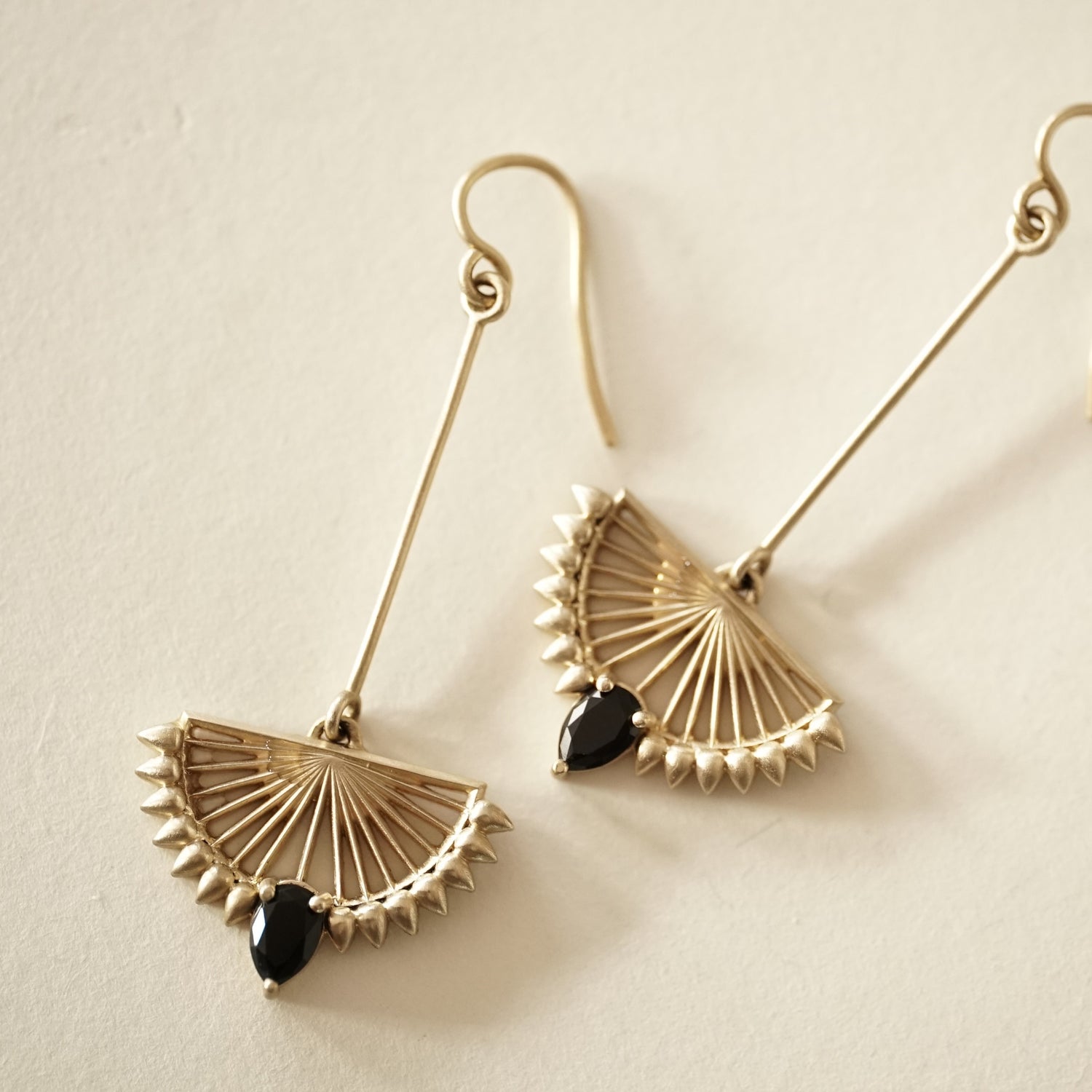 A pair of deco inspired matte finish yellow gold drop earrings with pear shape black onyx on a matte white background