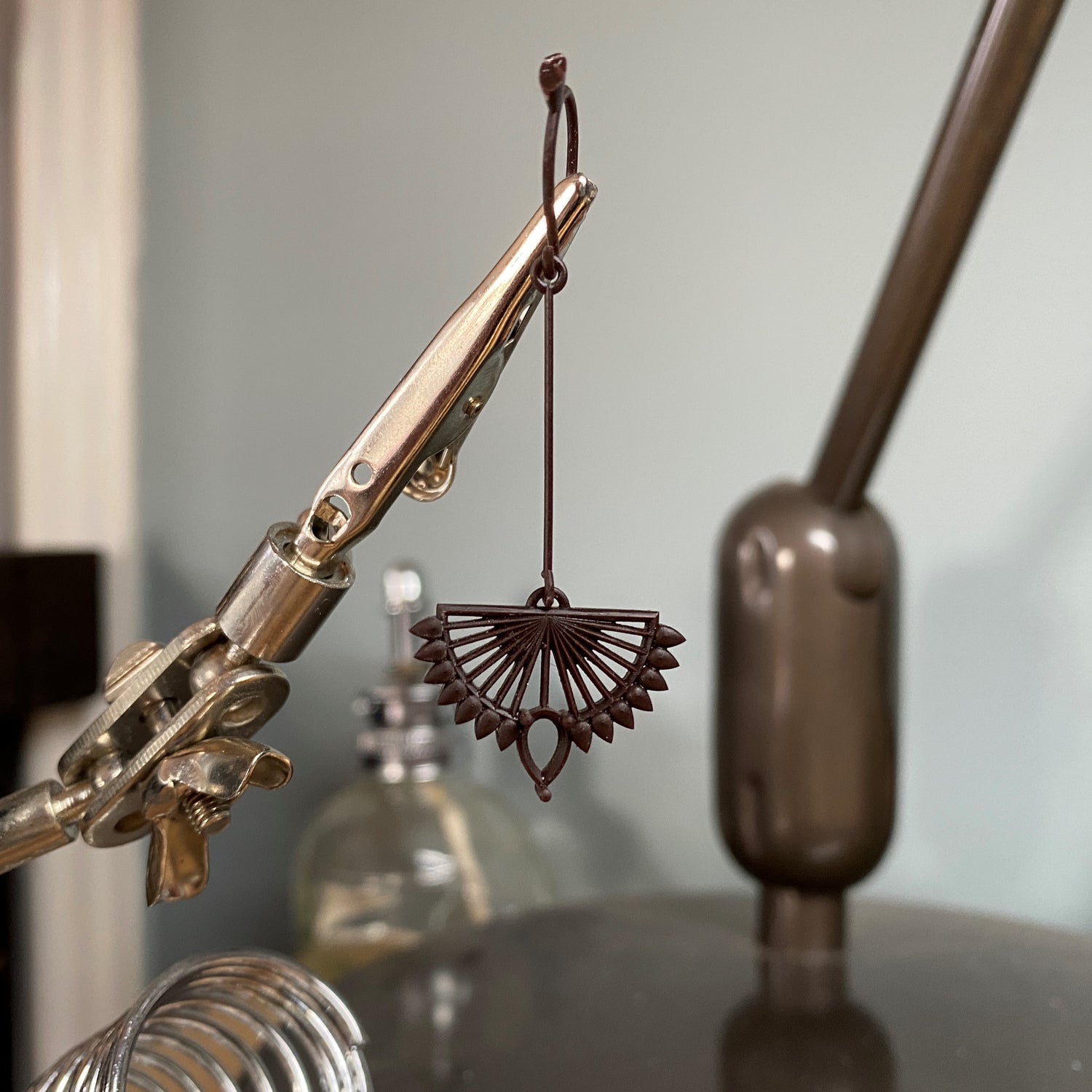 A 3d printed wax model of an art deco inspired earring is suspended in a helping hands bench tool