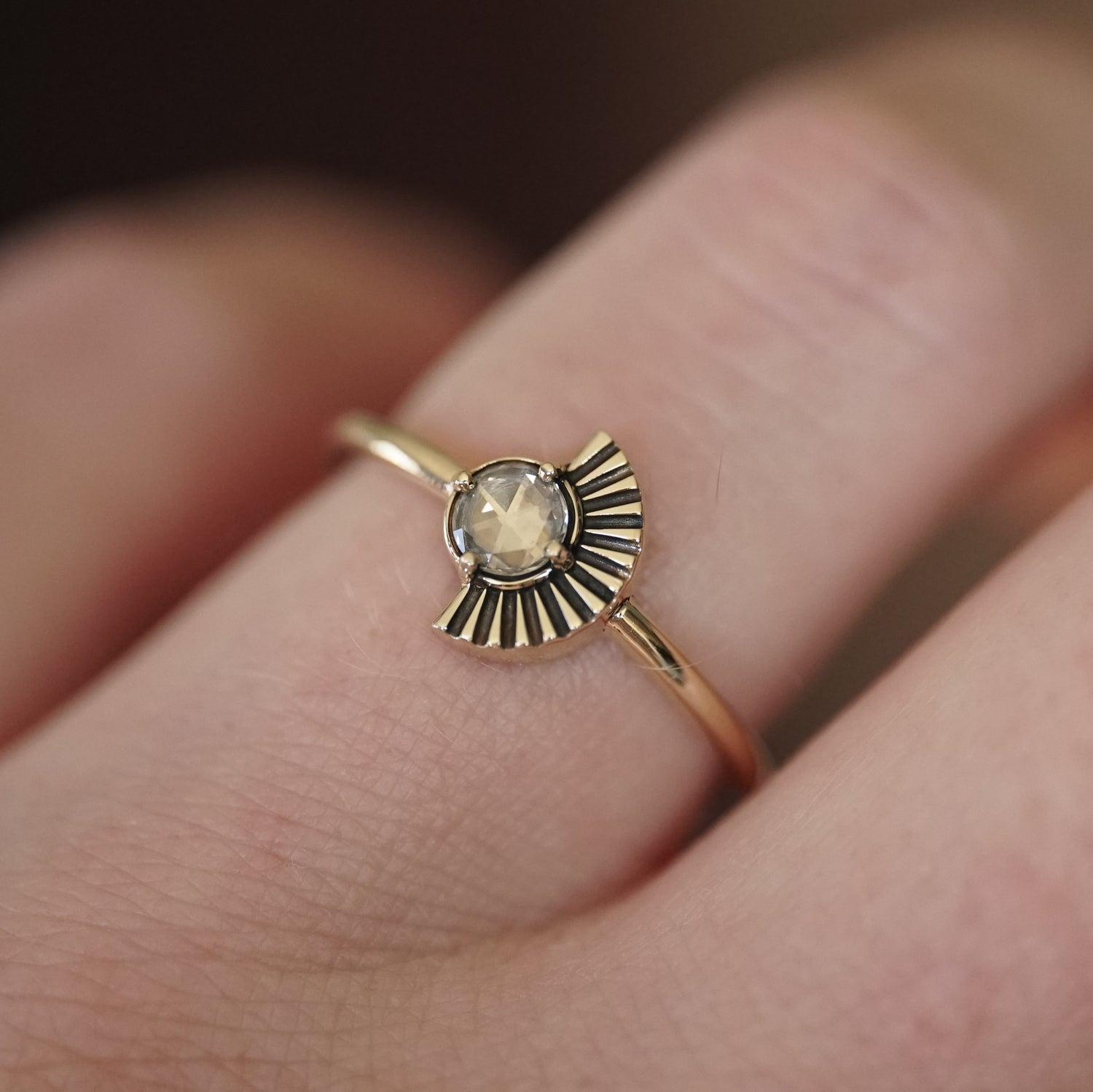 a rose cut white diamond in a yellow gold ring with an art deco fan element to one side is shown on a light-skinned left hand
