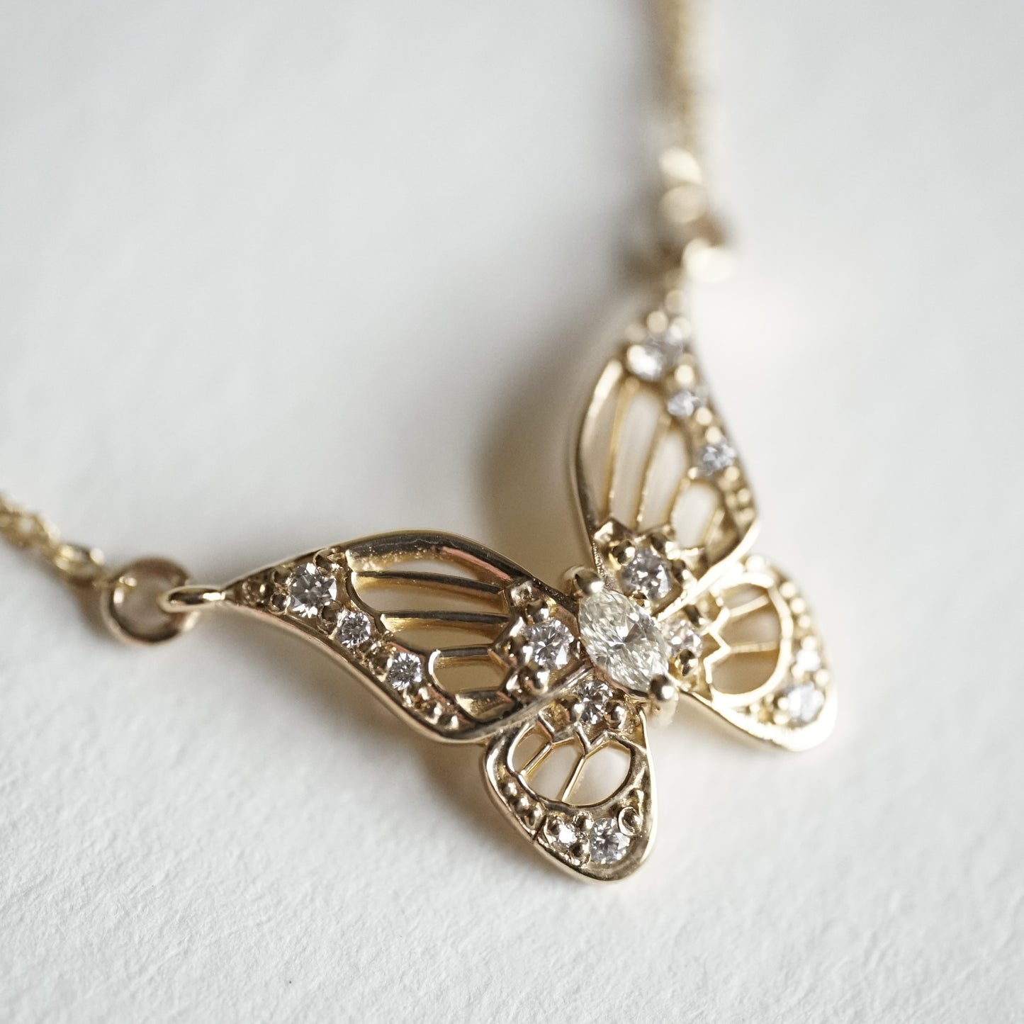 a macro photo of an art deco inspired butterfly pendant with a marquise diamond in the center and suspended on a sparkly chain
