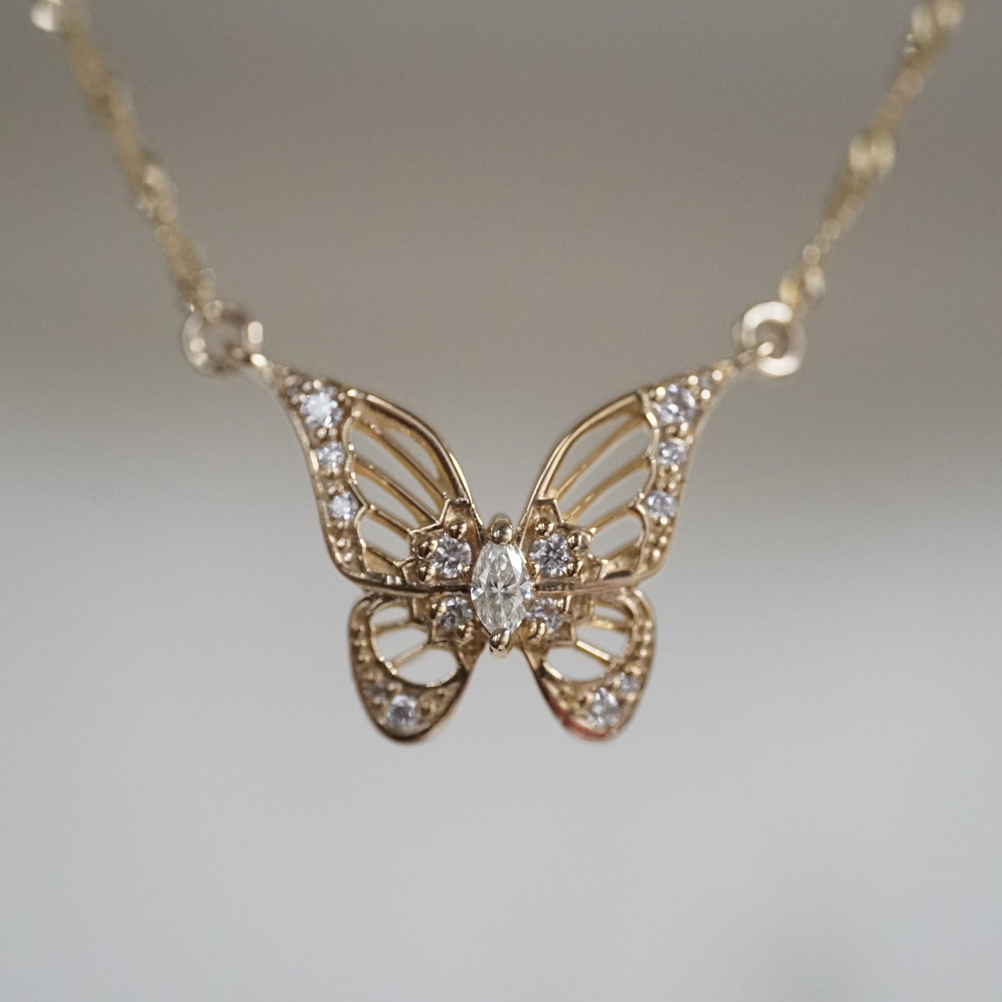 a macro photo of an art deco inspired butterfly pendant with a marquise diamond in the center and suspended on a sparkly chain