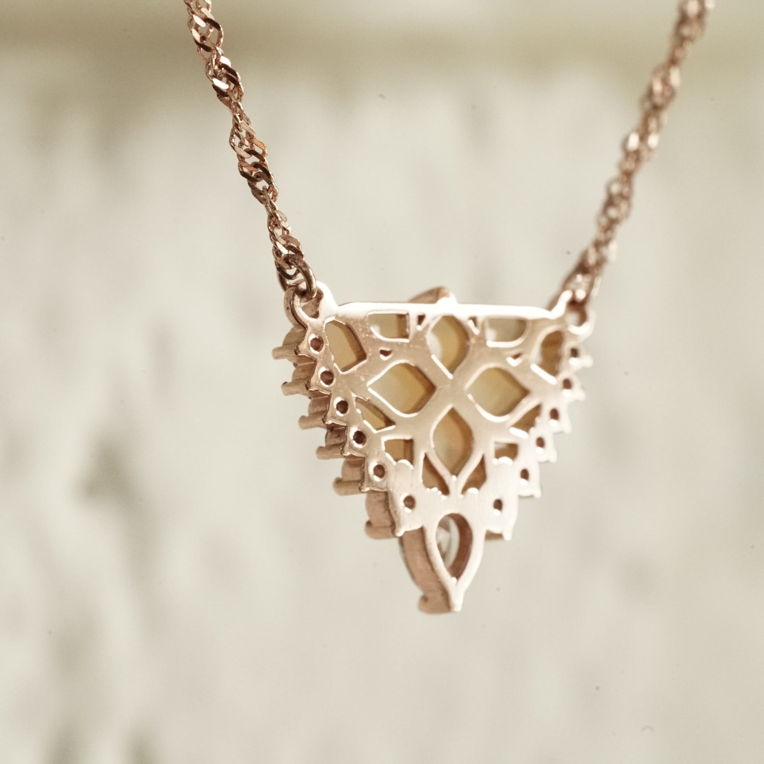a rose gold necklace with a triangular shape opal center stone and diamond accents of graduated sizes rotated to show the backside of the pendant