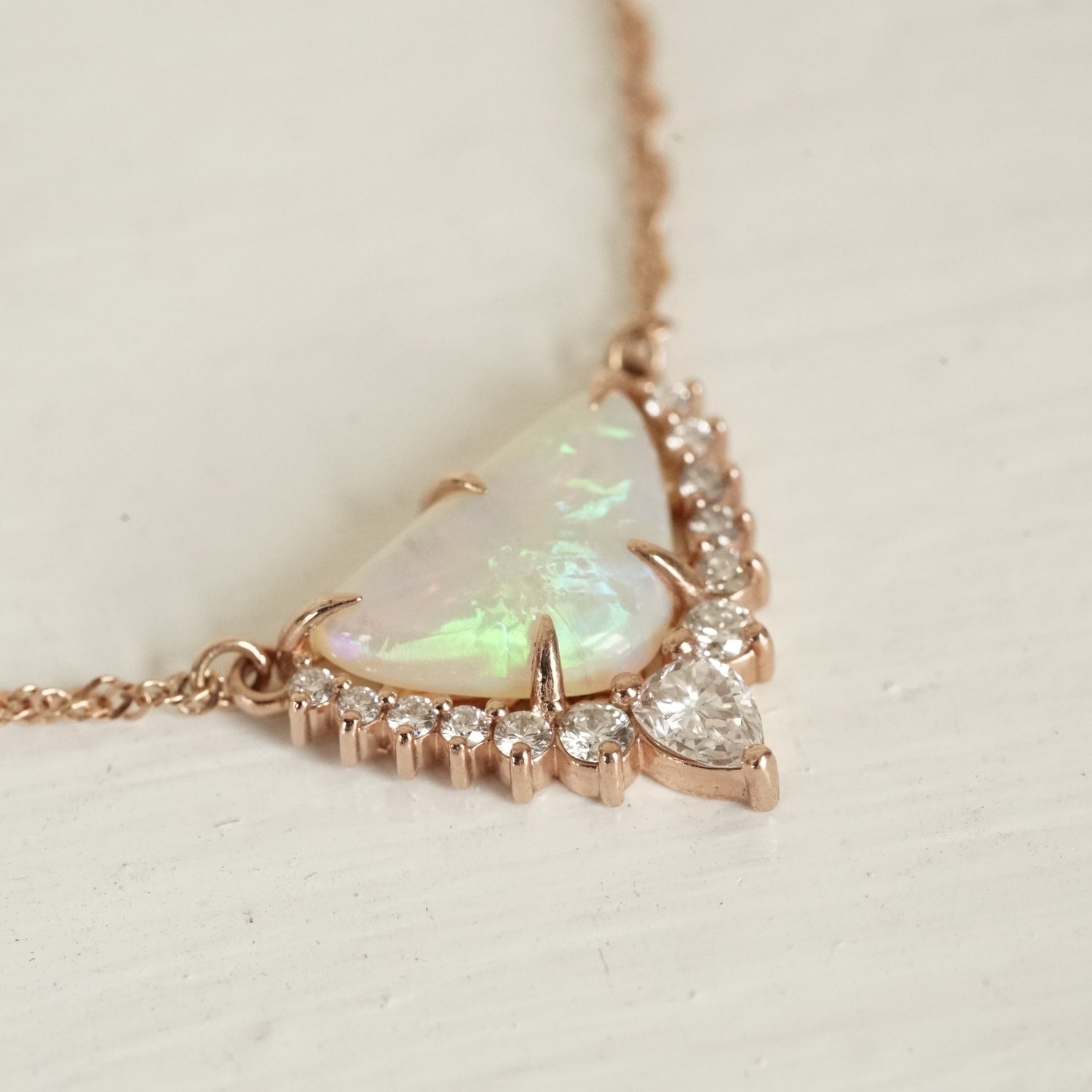 a rose gold necklace with a triangular shape opal center stone and diamond accents of graduated sizes on a glossy white background