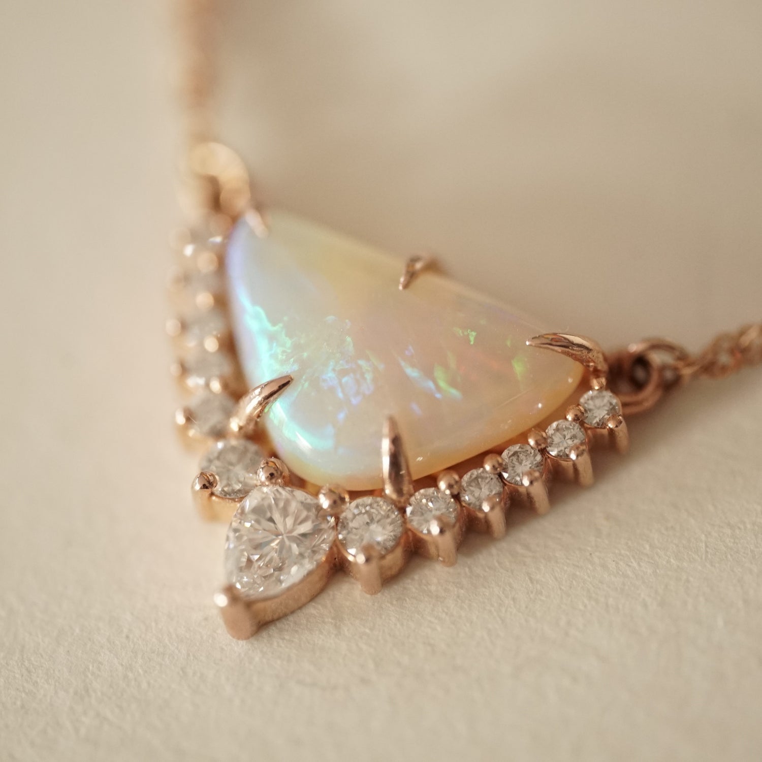 a rose gold necklace with a triangular shape opal center stone and diamond accents of graduated sizes on a matte white background