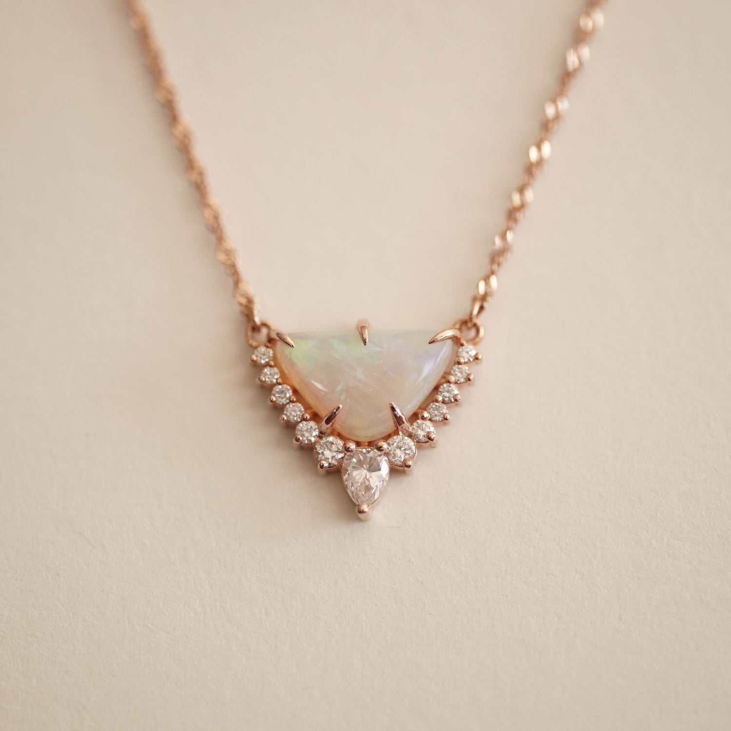 a rose gold necklace with a triangular shape opal center stone and diamond accents of graduated sizes on a matte white background