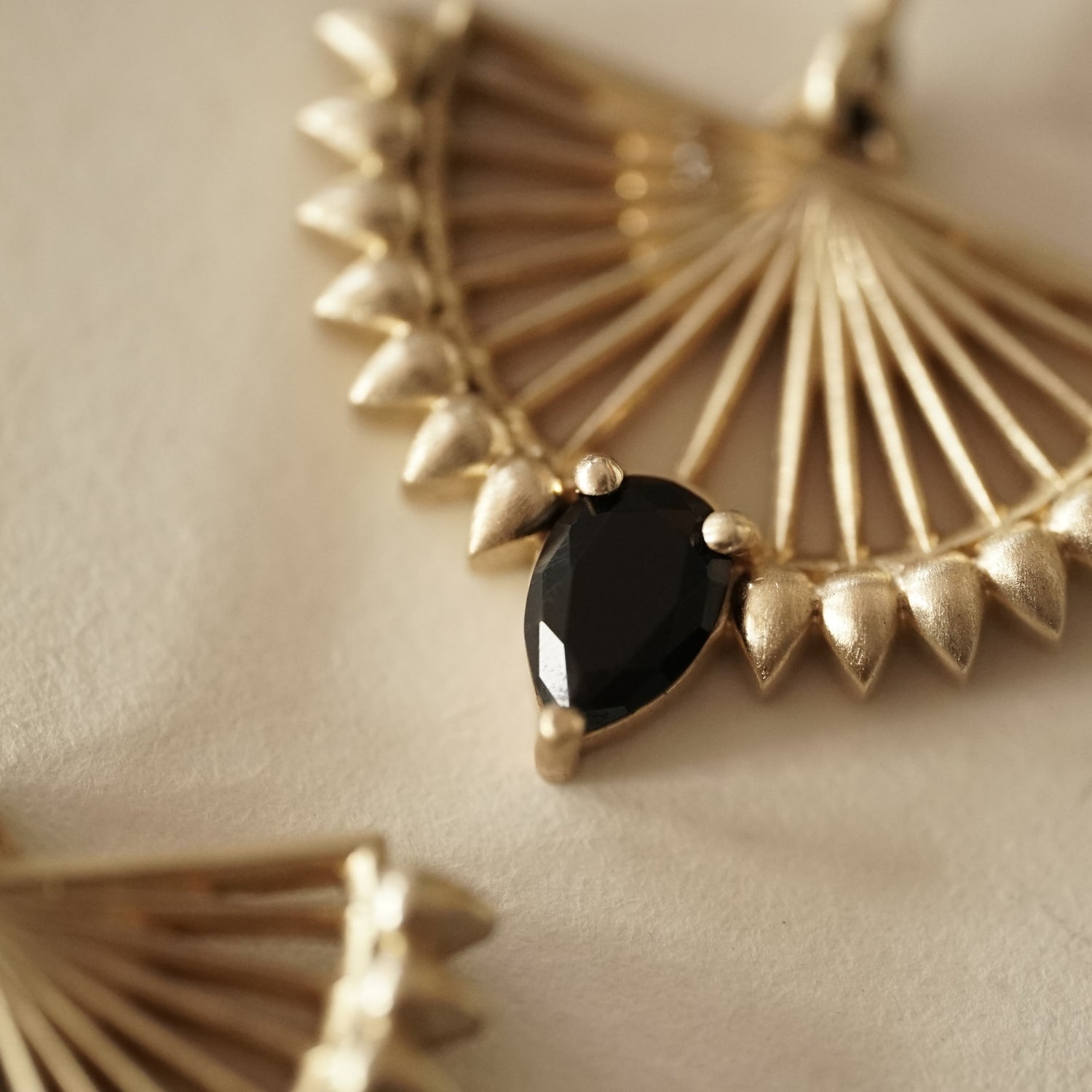 a macro photo of a pear shape black onyx set in an art deco inspired yellow gold earring
