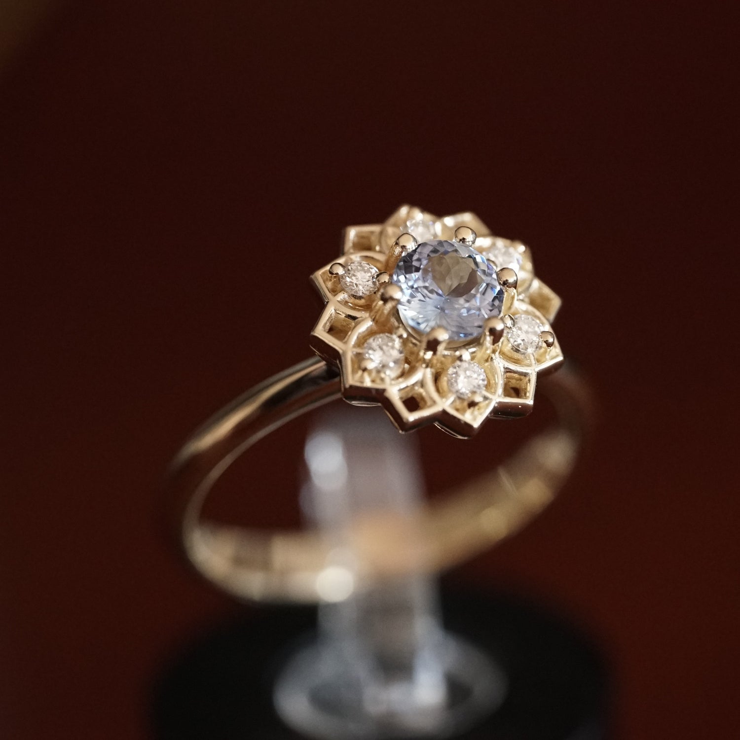 a yellow gold ring with a light blue sapphire enter stone and 6 white diamond accents in an open wire floral design