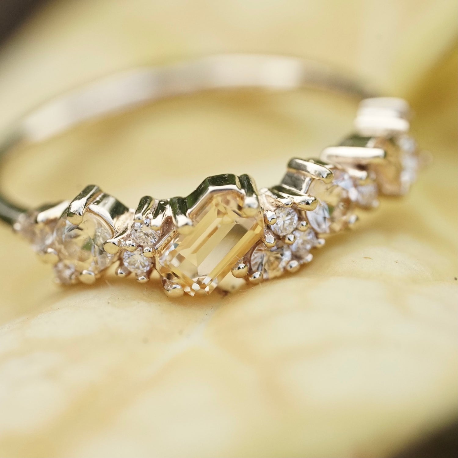 a macro photo of a yellow gold ring with yellow gems of mixed cuts and sizes are paired with white diamonds on a yellow background