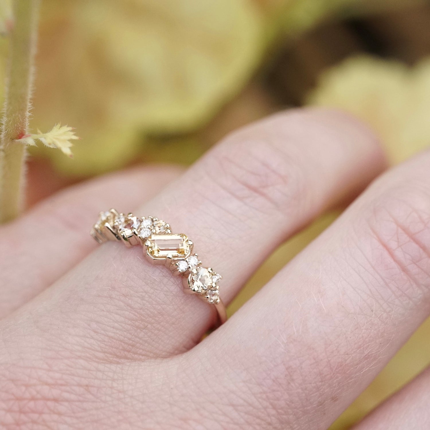 a yellow gold ring with yellow gems of mixed cuts and sizes are paired with white diamonds on a light skinned left hand